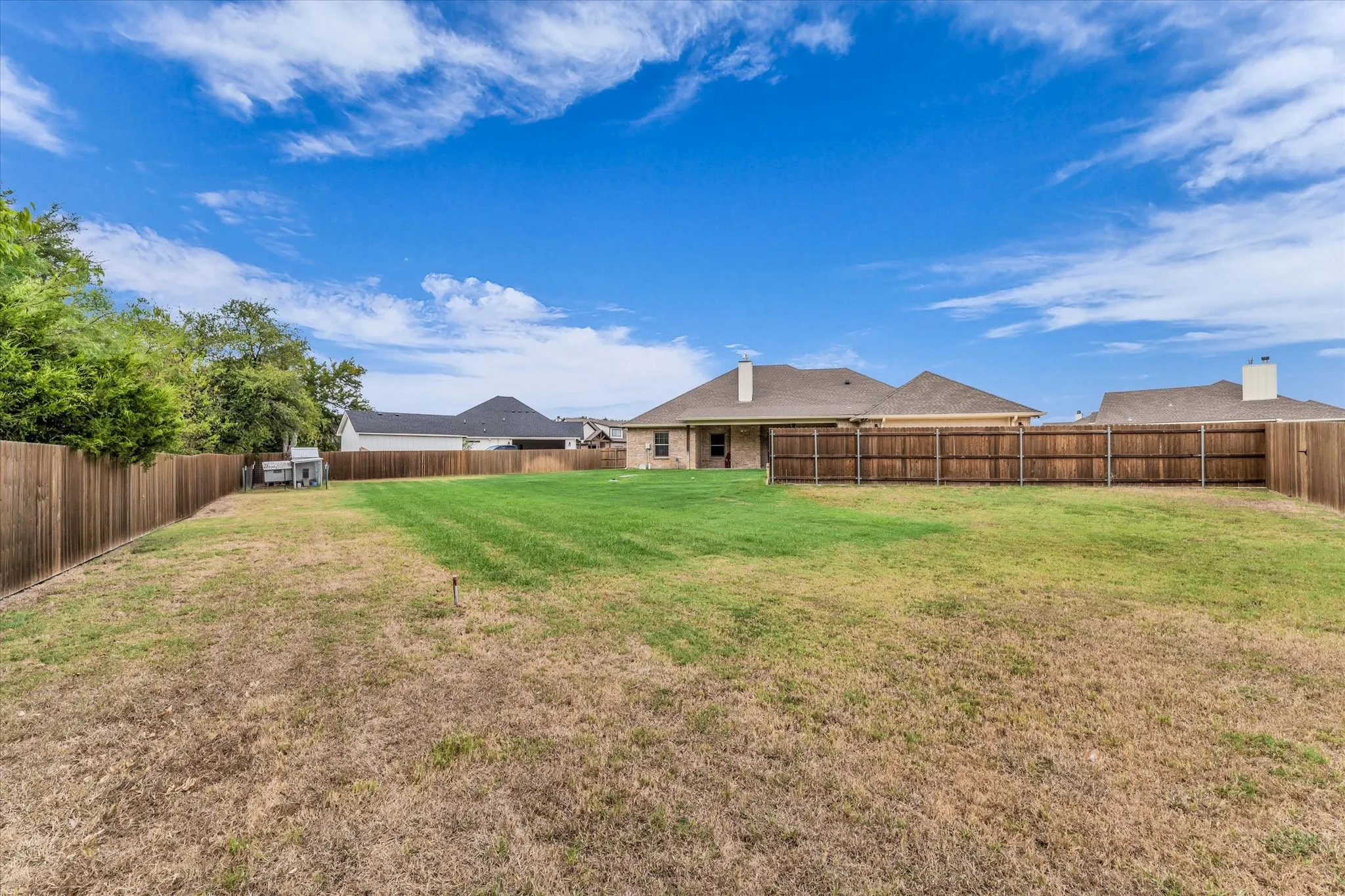 Expansive backyard featuring a partial manicured lawn, wood fencing, and a brick exterior home