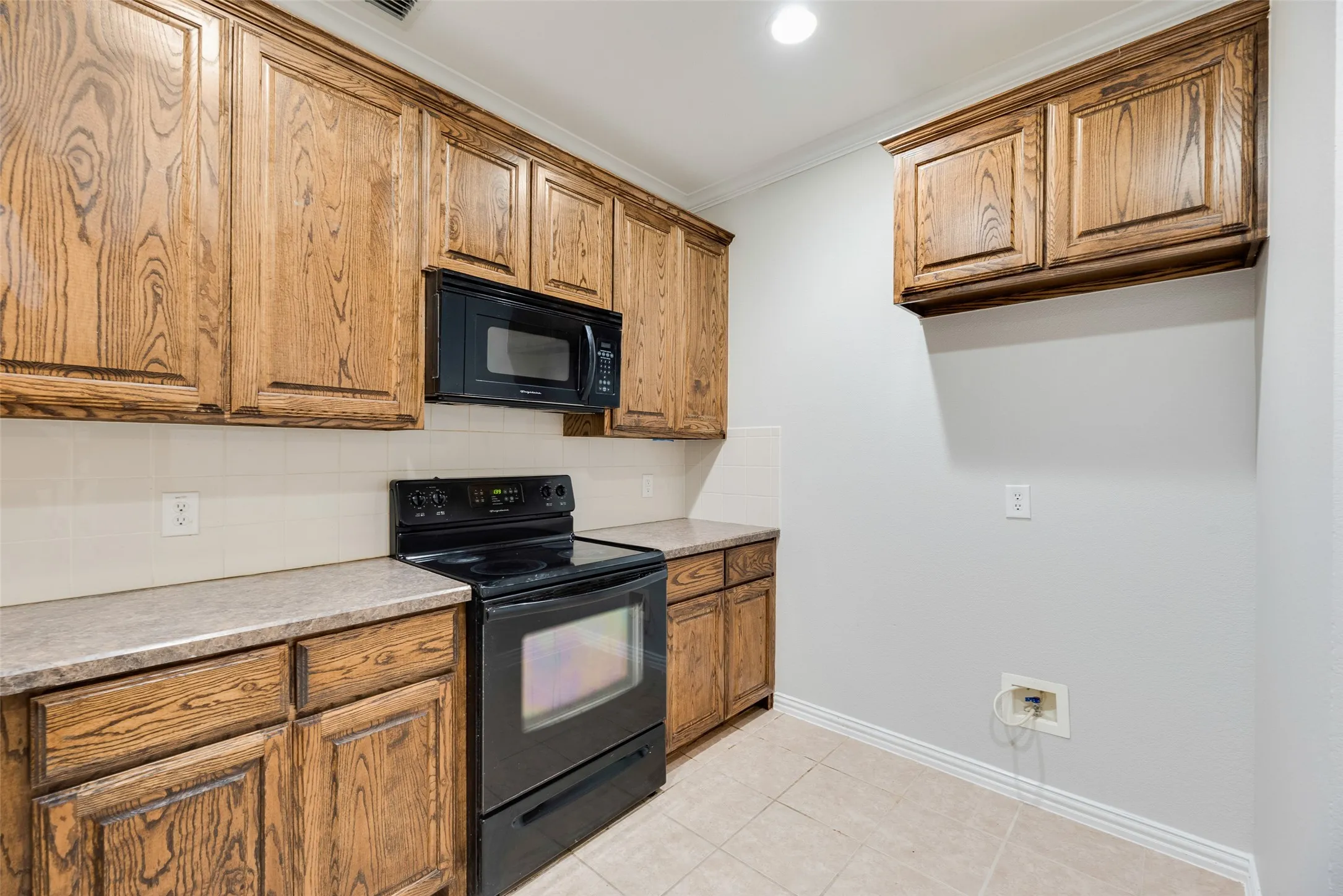 Kitchen featuring wood cabinetry, solid surface countertops, black appliances, a tile backsplash, and tile flooring