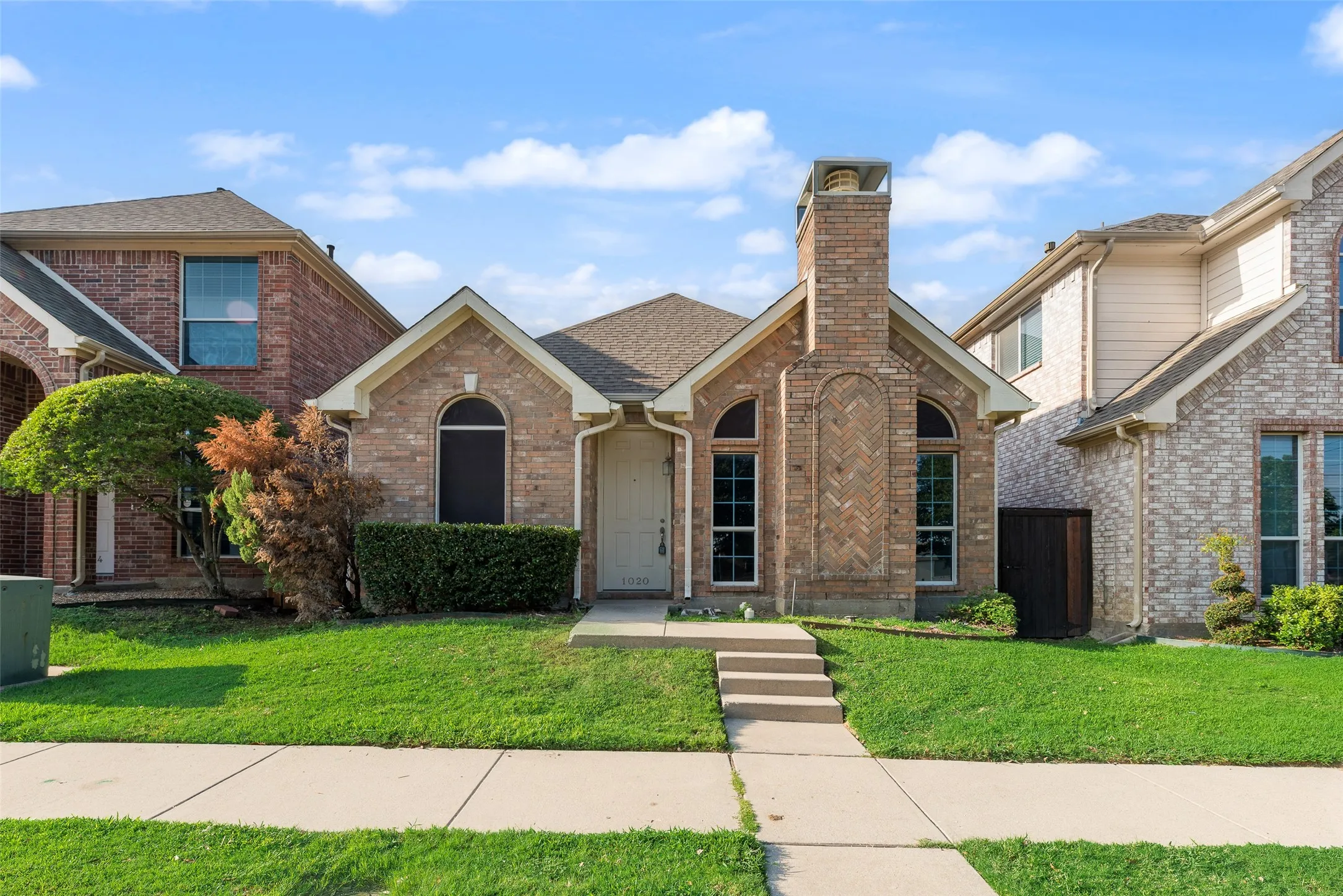 Brick exterior with a prominent chimney, arched windows, and a concrete pathway