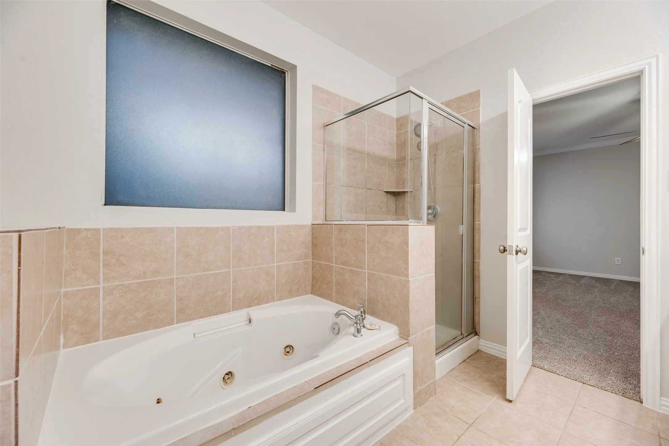 Tiled bathroom featuring a built-in jetted tub, a glass-enclosed shower, and a privacy window
