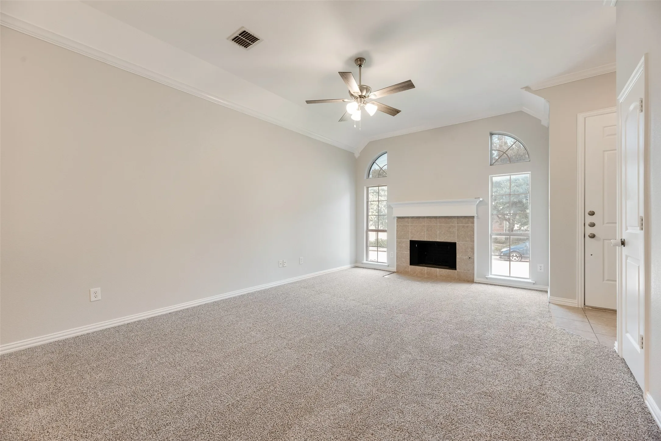 Living area featuring high ceilings, a ceiling fan, arched windows, a fireplace with a tile surround and mantel, and carpet flooring