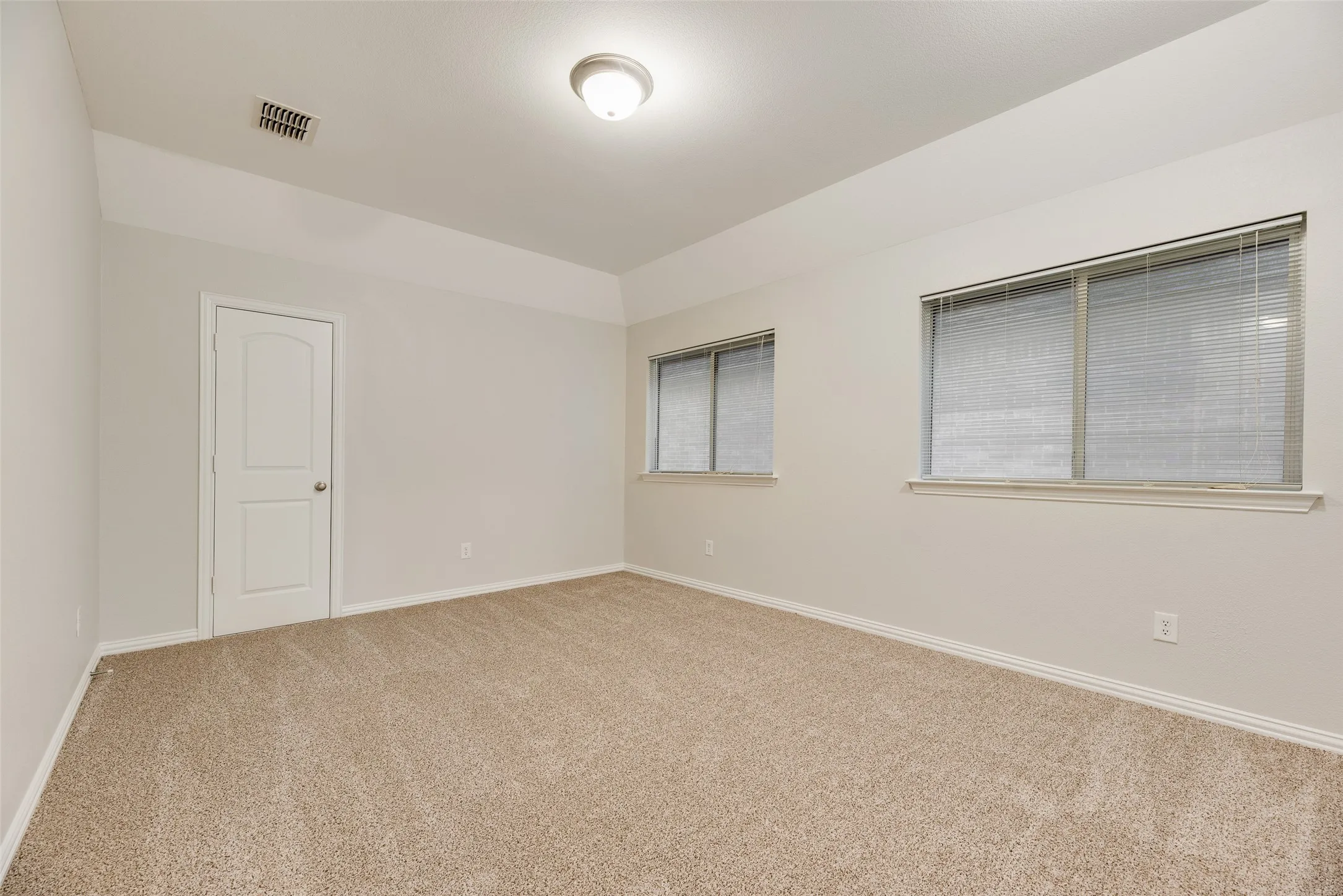 Textured carpet flooring, neutral paint palette, two windows with blinds, recessed ceiling light fixture, and panel door