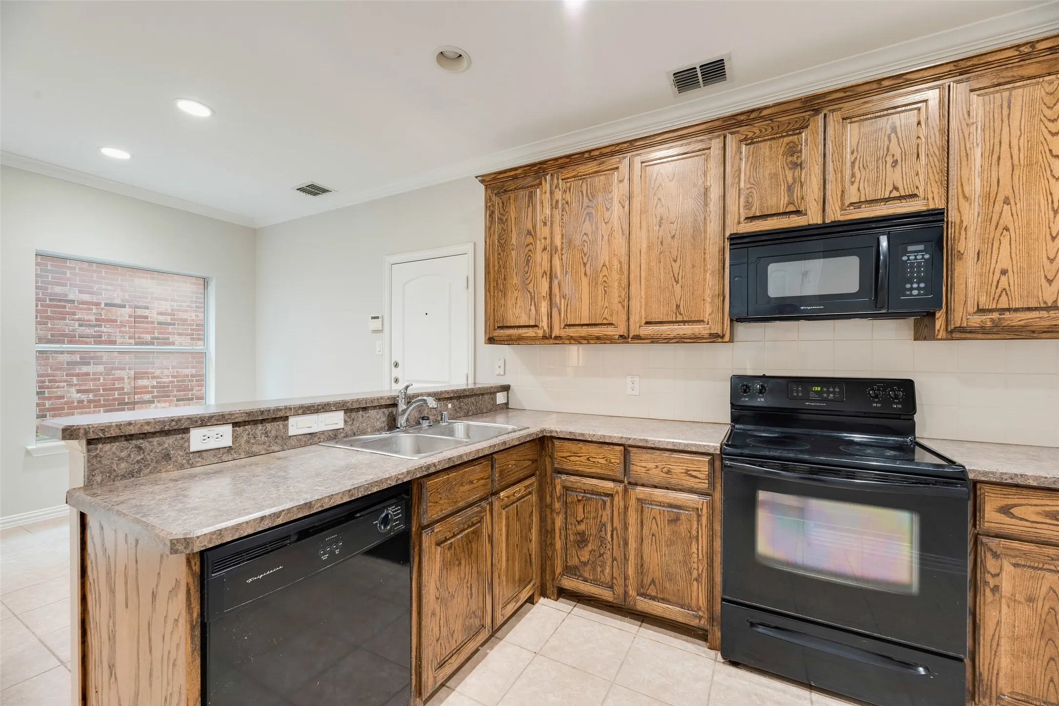 Galley kitchen featuring wood-finish cabinetry, granite countertops, black appliances including a slide-in range and over-the-range microwave, tile flooring, and a window overlooking the exterior