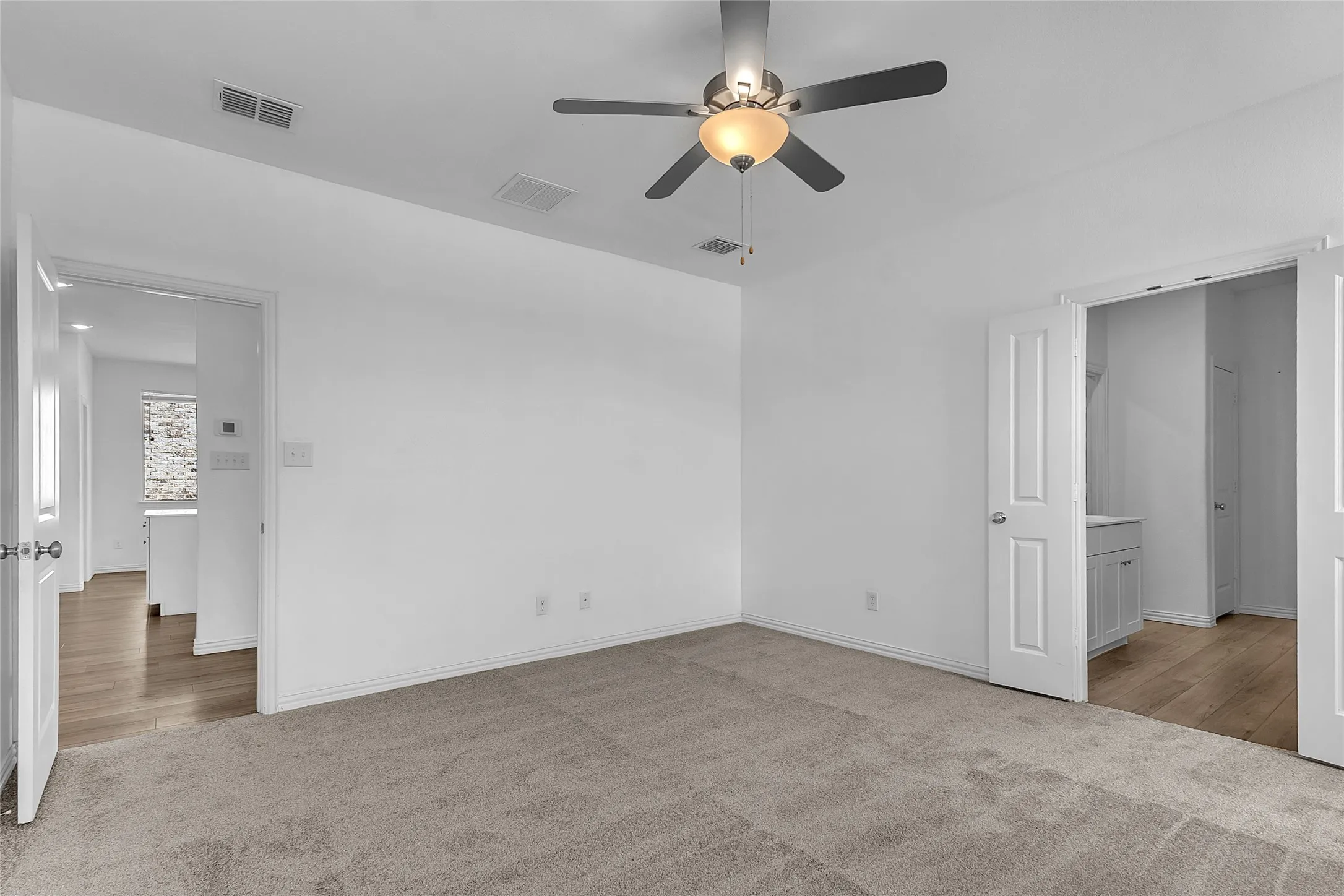 Primary bedroom with carpet and a ceiling fan, a door to the living area, and double doors to the primary bath