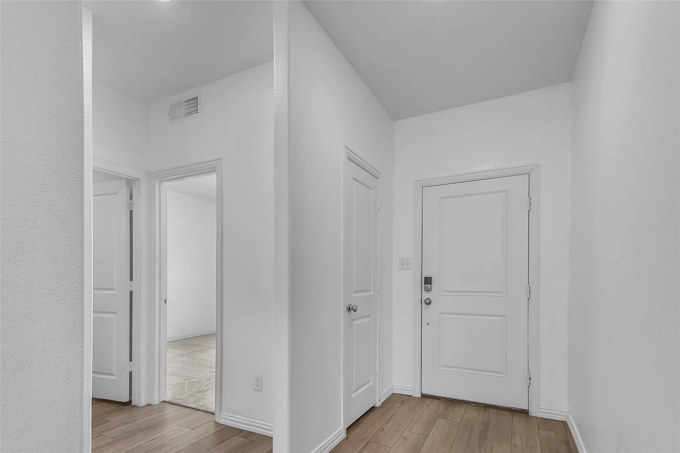 Entry foyer with wood-look flooring, a paneled front door, and doors leading to a secondary bedroom and closets