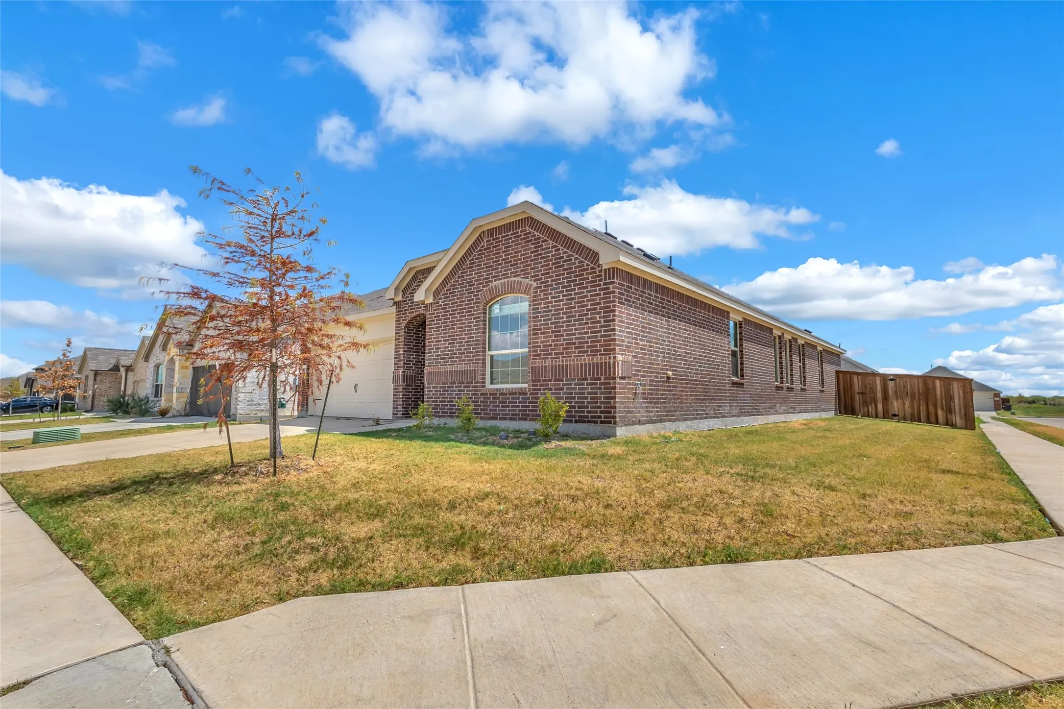 Side view of the corner-lot home showing the brick exterior, arched window, and fenced side yard