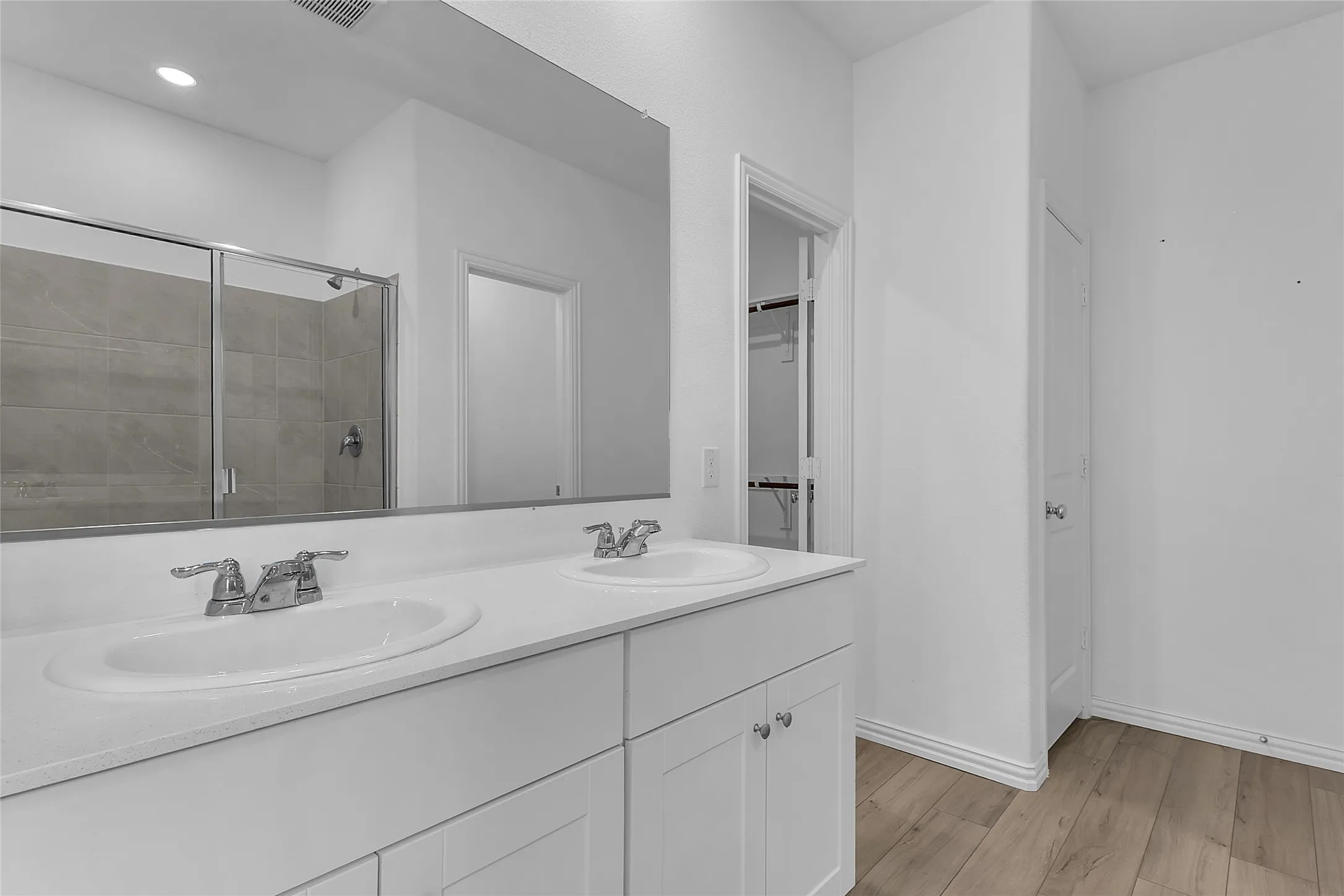 Primary bath with a double vanity, wide mirror, and a walk-in closet with wire shelving just beyond