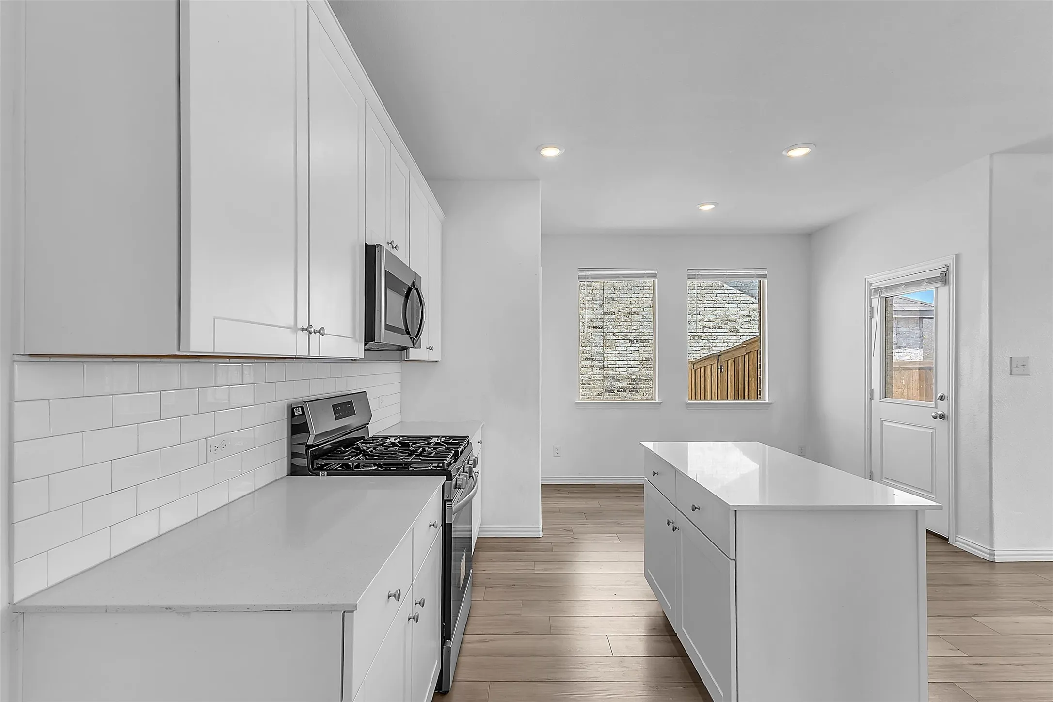Kitchen with white shaker-style cabinets, subway tile backsplash, a gas range, center island, and nook with back door