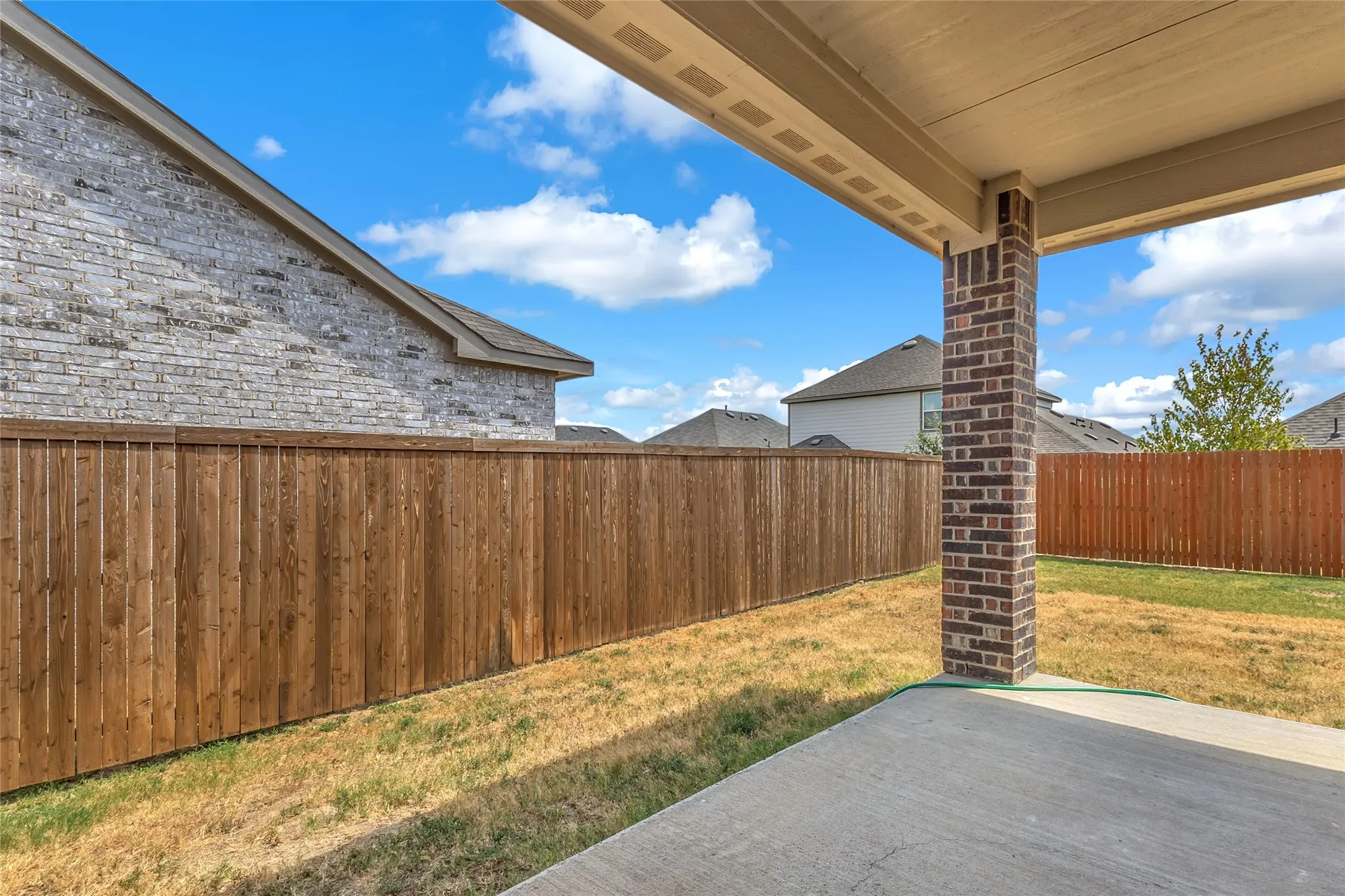 Covered back patio with a brick column, overlooking the grassy backyard and wood privacy fence