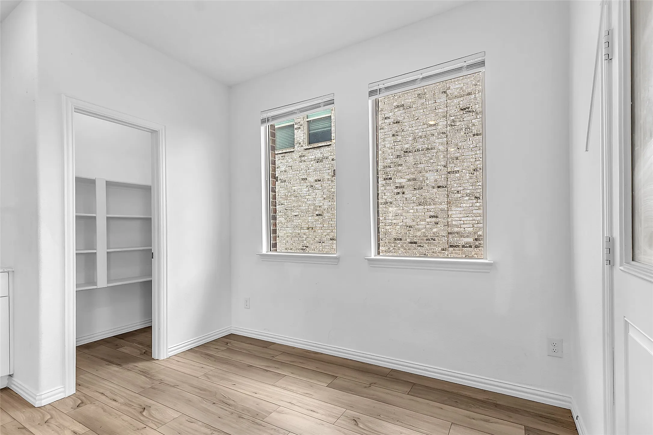 Breakfast nook with two windows, wood-look floors, and a pantry with built-in shelving just off the kitchen