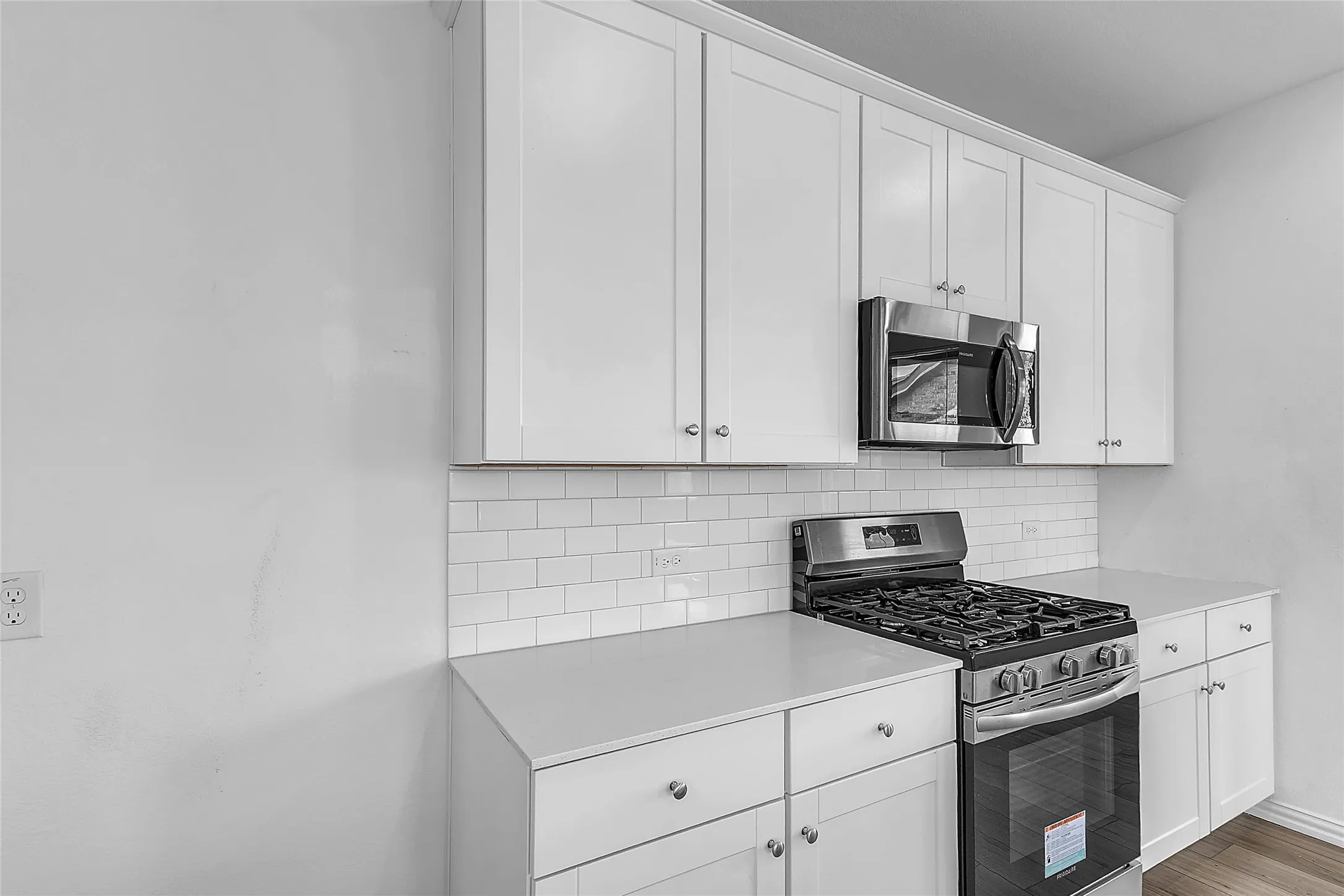 Gas range with five burners, over-range microwave, white cabinets, and a white subway tile backsplash