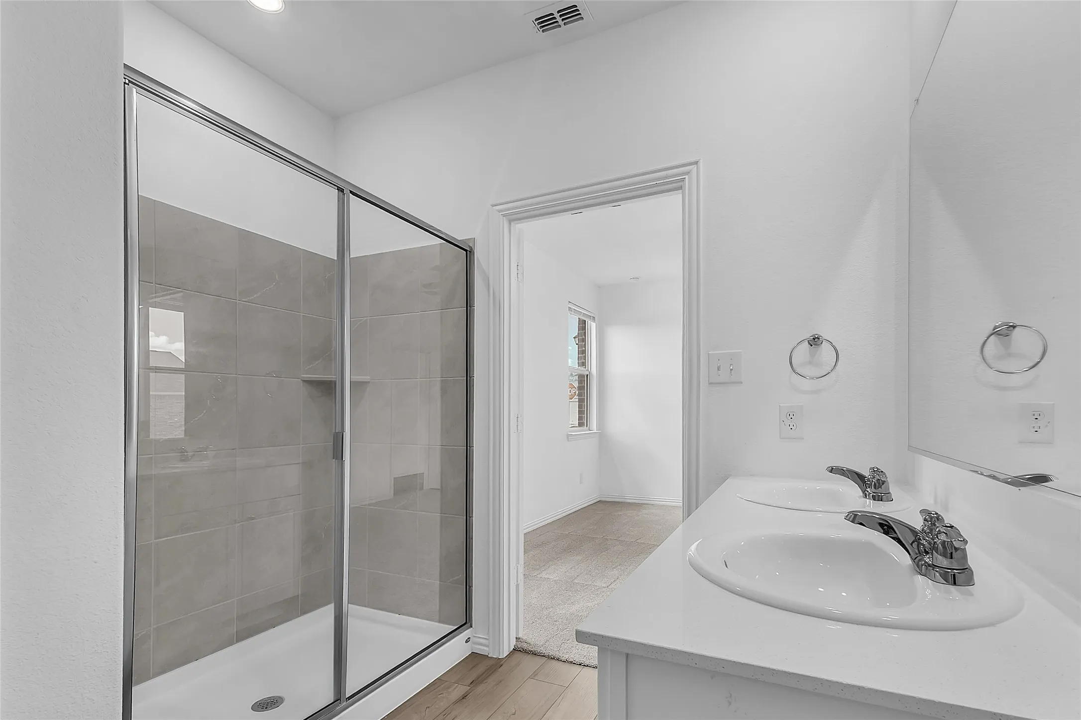 Primary bath with a glass-enclosed shower and built-in niche, dual sinks, and a door back to the bedroom