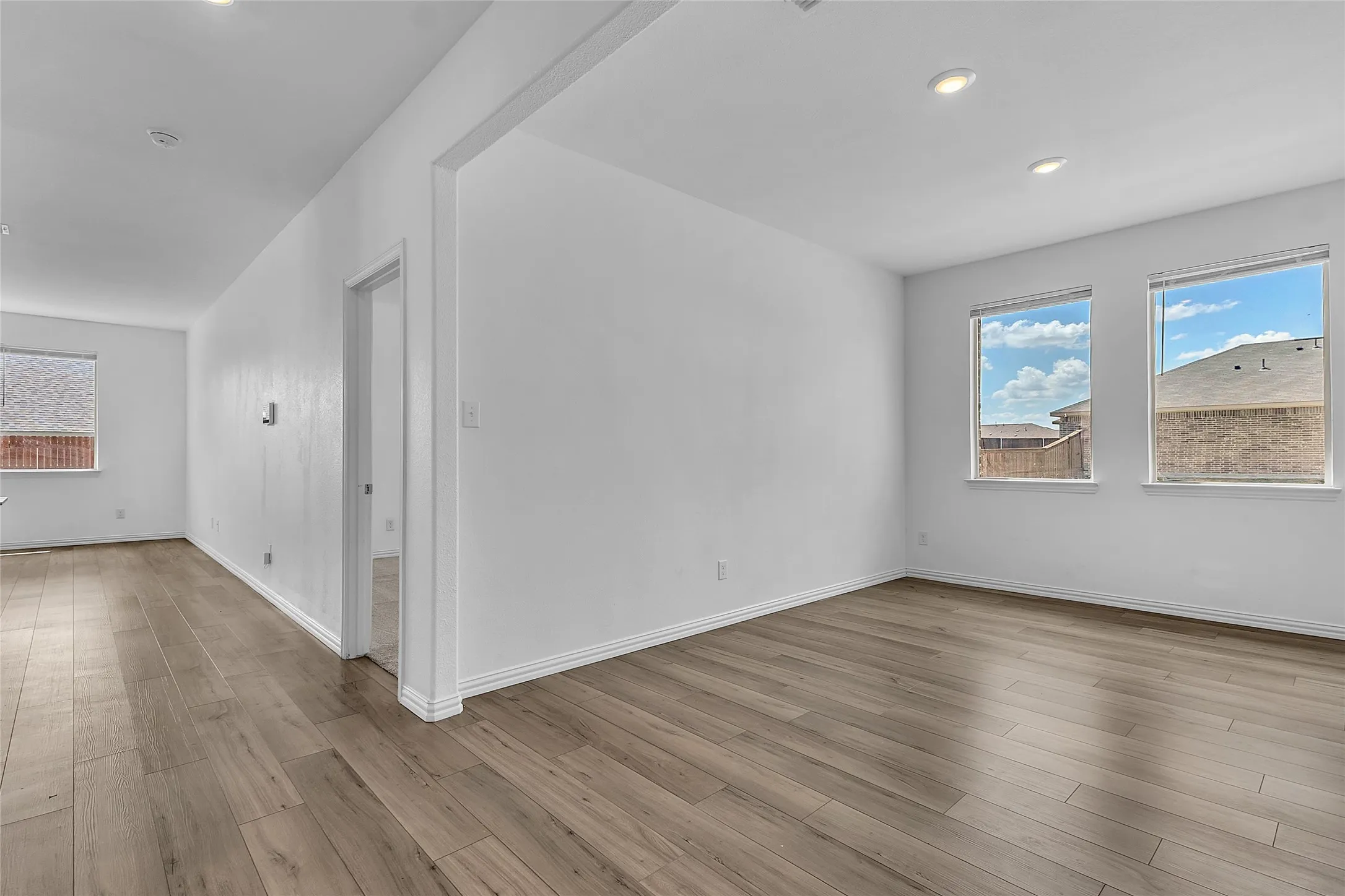 Dining room off the front hall with recessed lighting, two windows, and wood-look floors that continue down the hallway