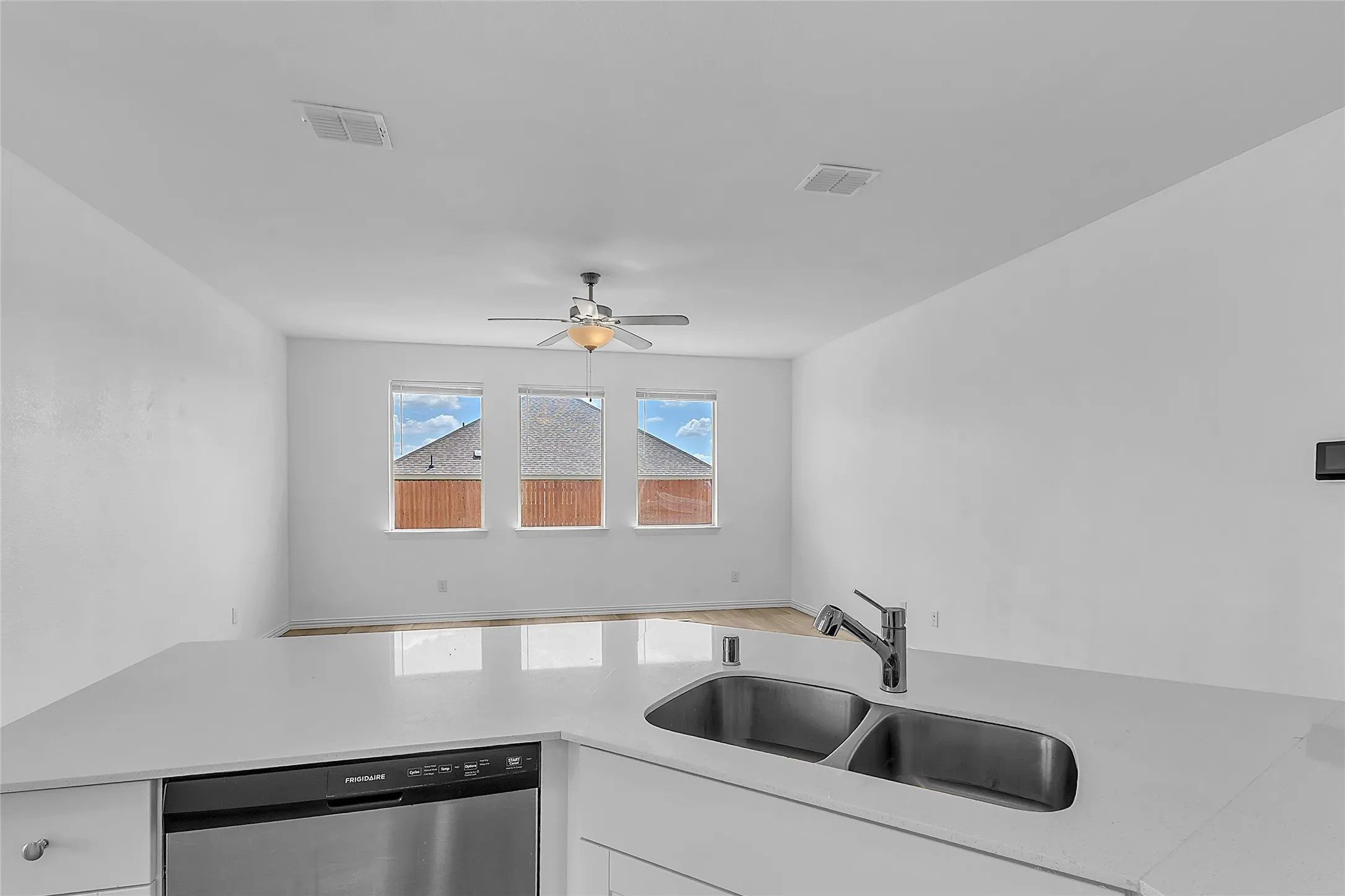 Kitchen peninsula with a double-basin sink and dishwasher, overlooking the living room's three windows