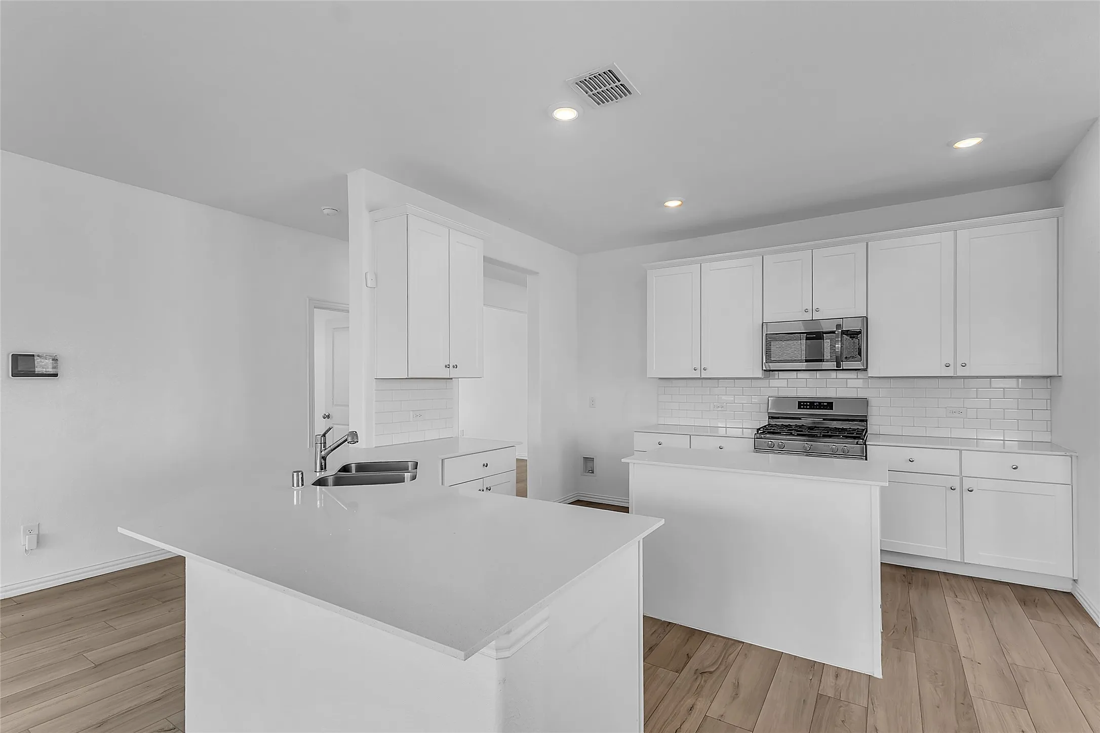 Open kitchen with a center island, sink peninsula, white cabinetry, and light counters in this Forney home