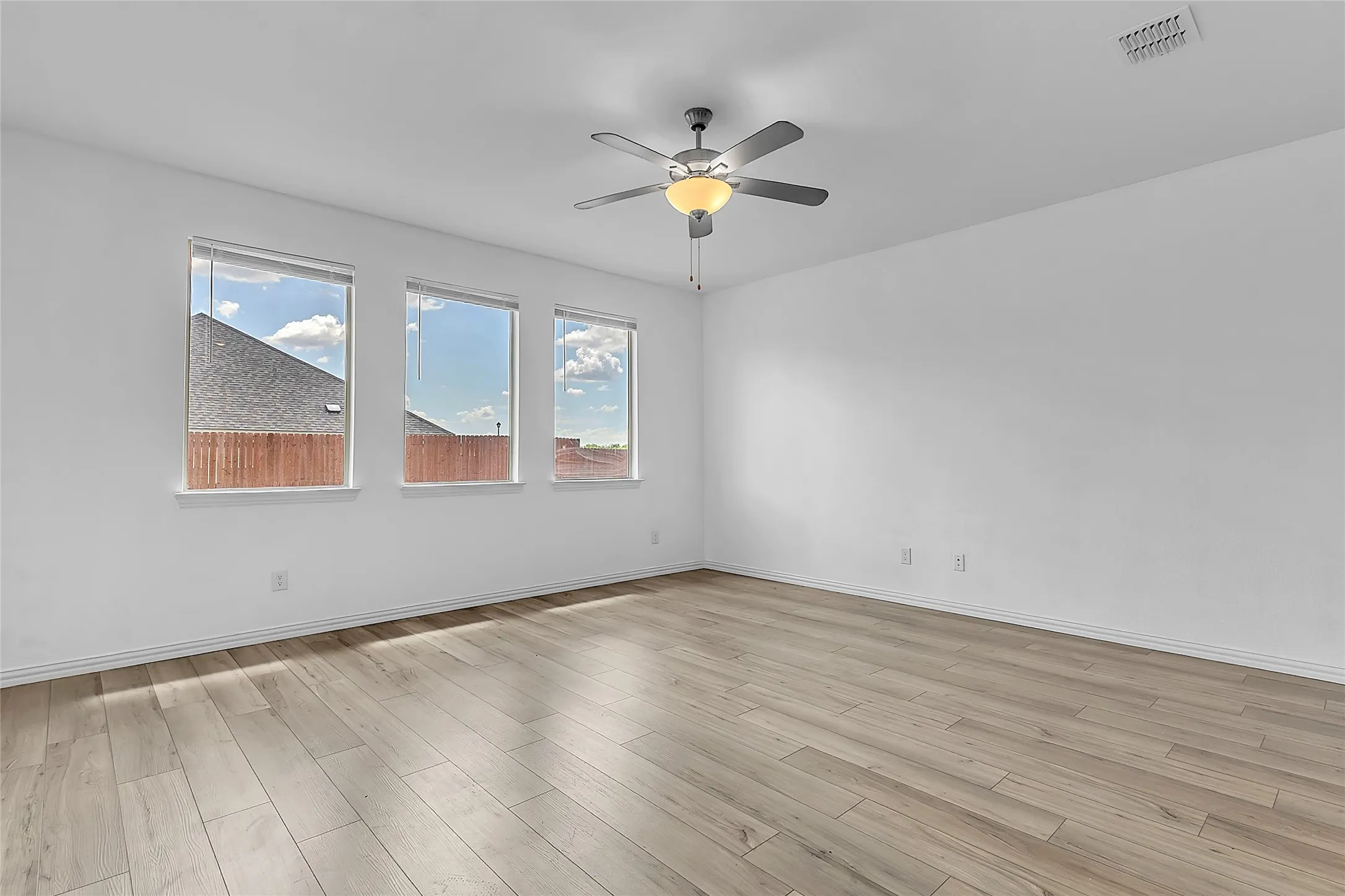Living room corner with three windows looking toward the fenced backyard, plus a ceiling fan with light kit