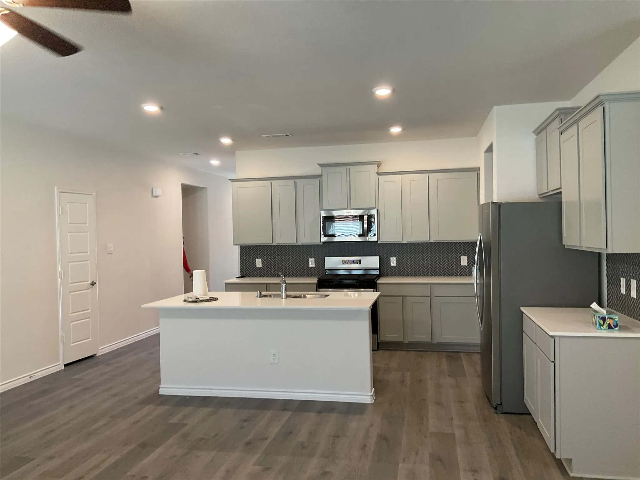 Kitchen with a kitchen island with sink, a sink, gray cabinetry, stainless steel appliances, and backsplash