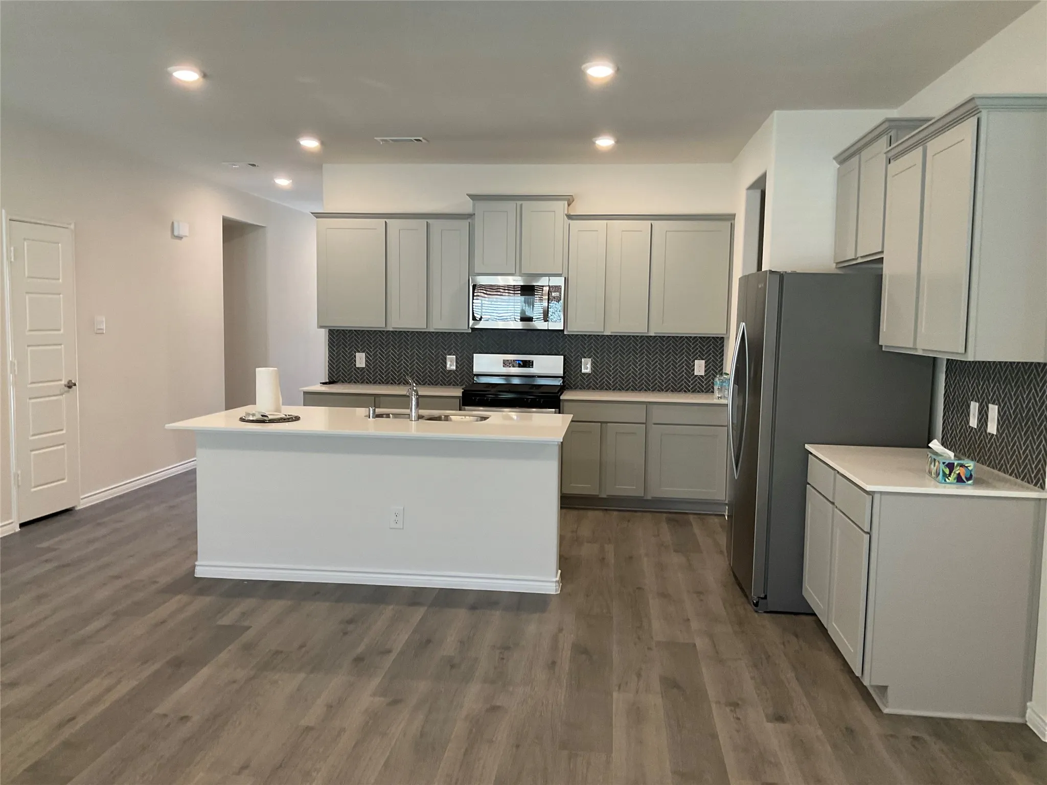 Kitchen featuring visible vents, gray cabinetry, an island with sink, stainless steel appliances, and a sink