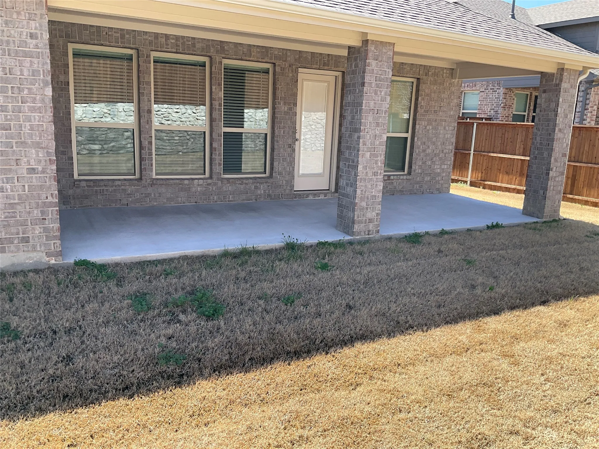 Doorway to property featuring a patio area, fence, brick siding, and roof with shingles