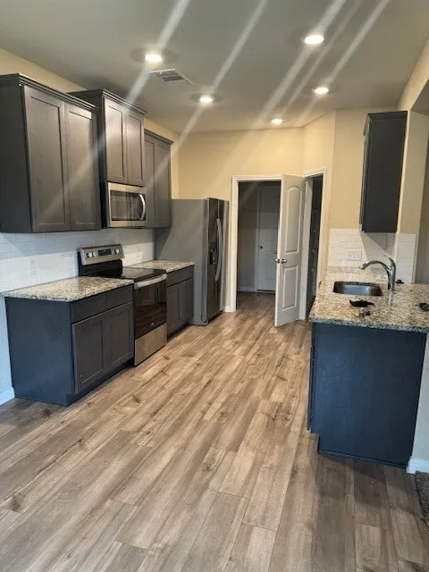 Modern kitchen featuring wood-finish flooring, dark cabinetry, and light-colored countertops