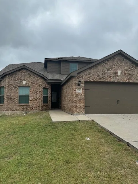 Brick veneer exterior with a brown garage door, dark shingle roof, and a concrete driveway