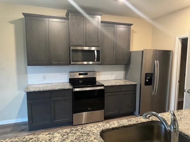 Kitchen featuring dark wood-finish cabinetry, stainless steel appliances, speckled stone countertops, and a subway tile backsplash
