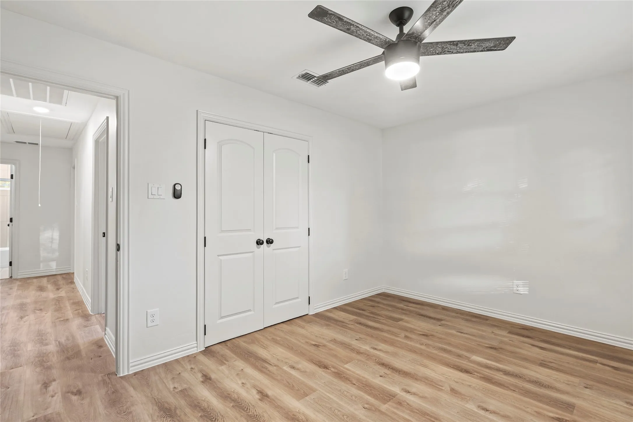 Unfurnished bedroom with attic access, light wood-style flooring, a closet, and baseboards