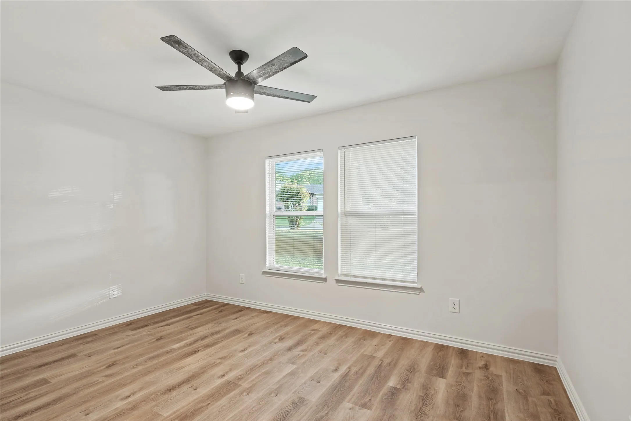 Empty room featuring light wood finished floors, baseboards, and a ceiling fan