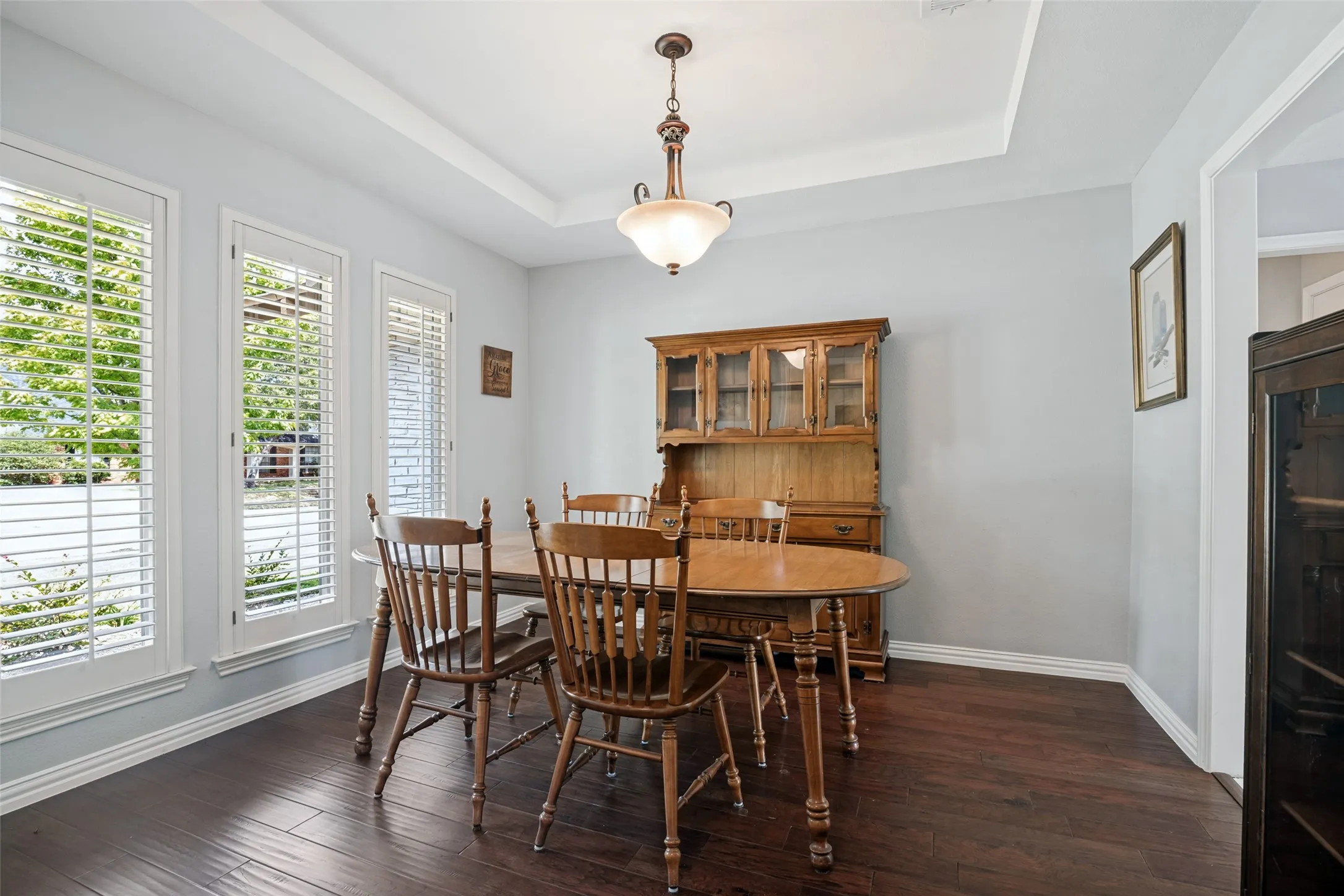 Hardwood-style flooring with white trim, a tray ceiling, and a prominent chandelier