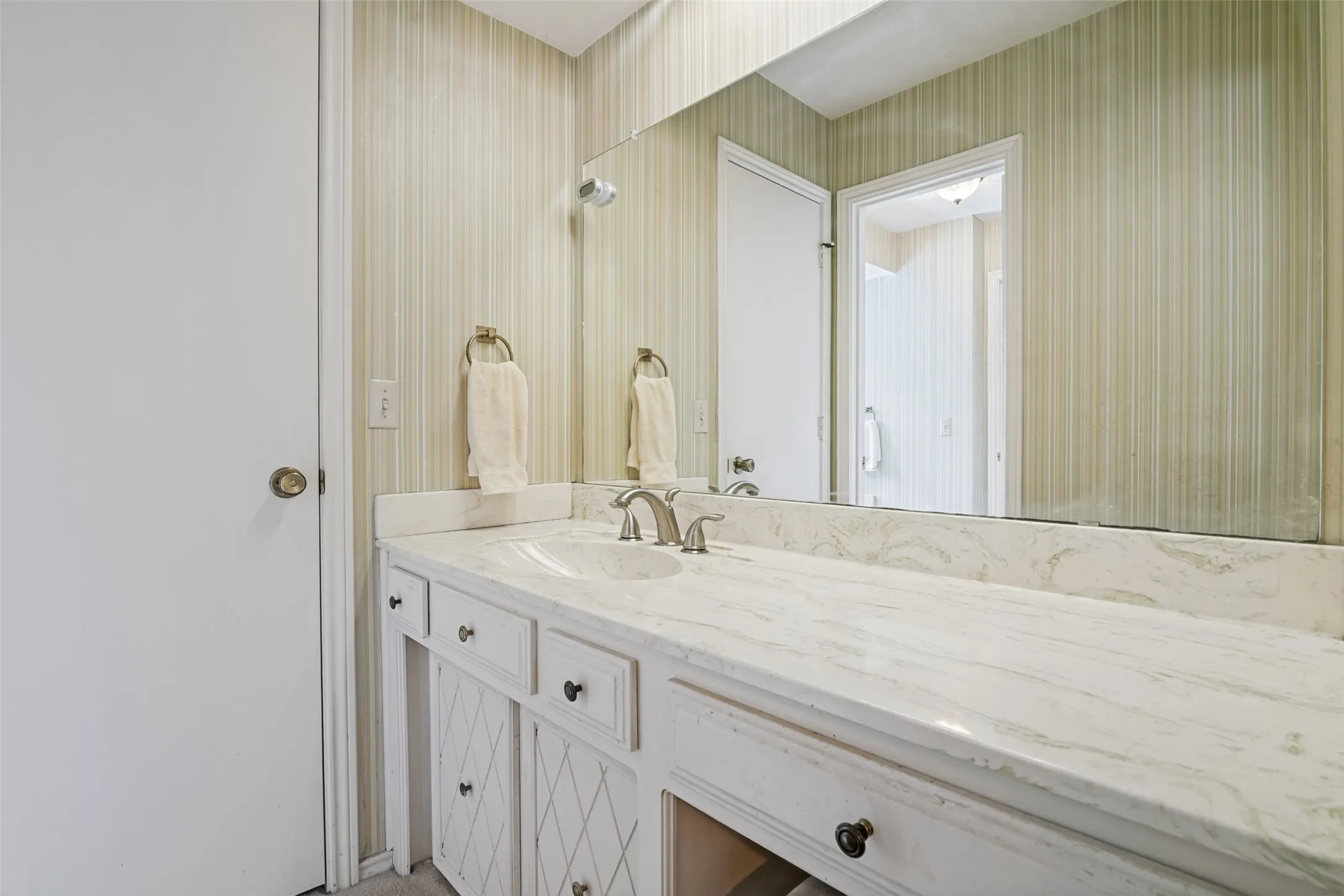 Vanity with an integrated sink, brushed nickel faucet, light-toned countertop, and white cabinetry with dark hardware
