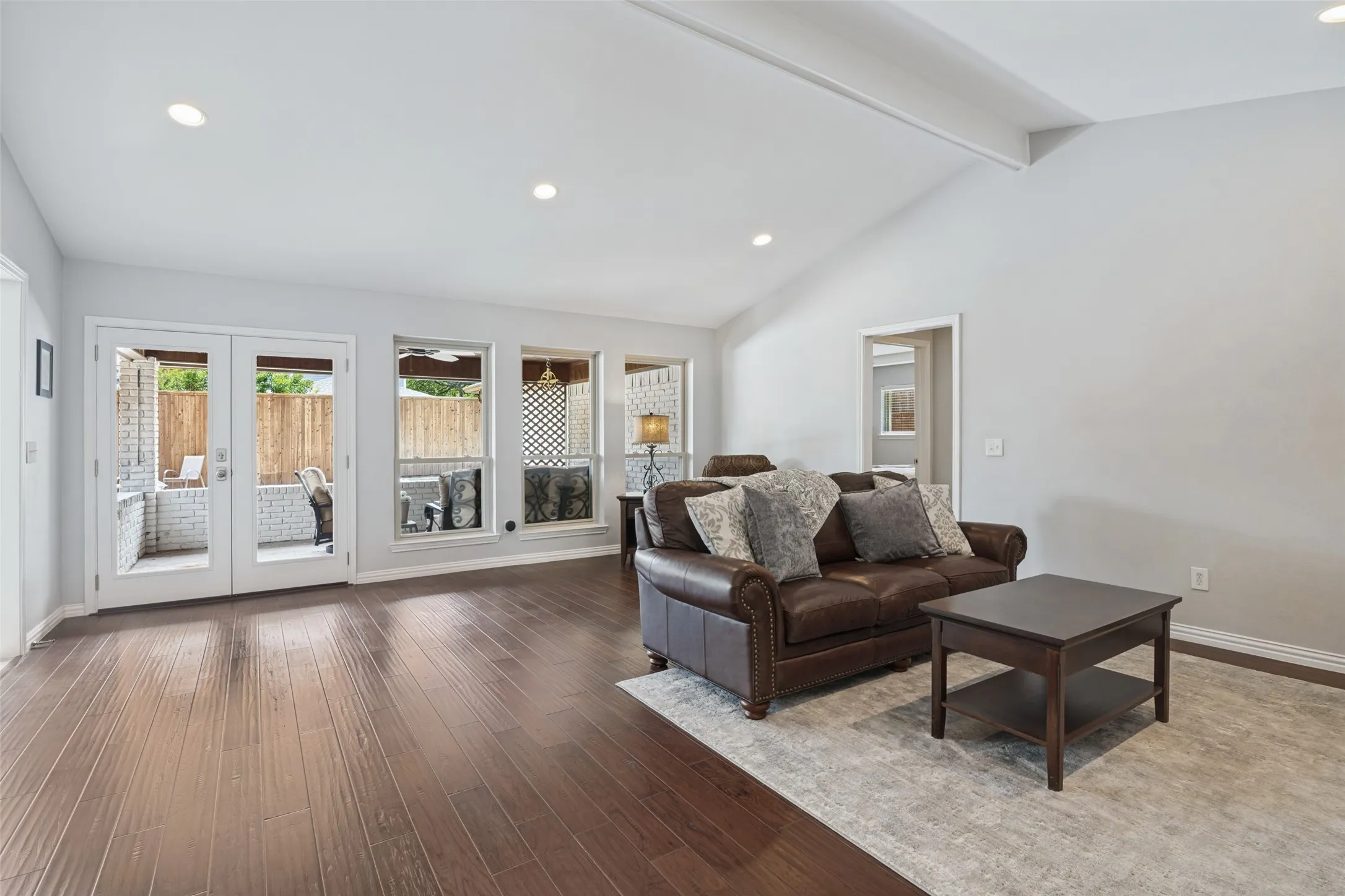 Wood-finish flooring throughout, vaulted ceiling, recessed lighting, and white French doors leading to a brick patio