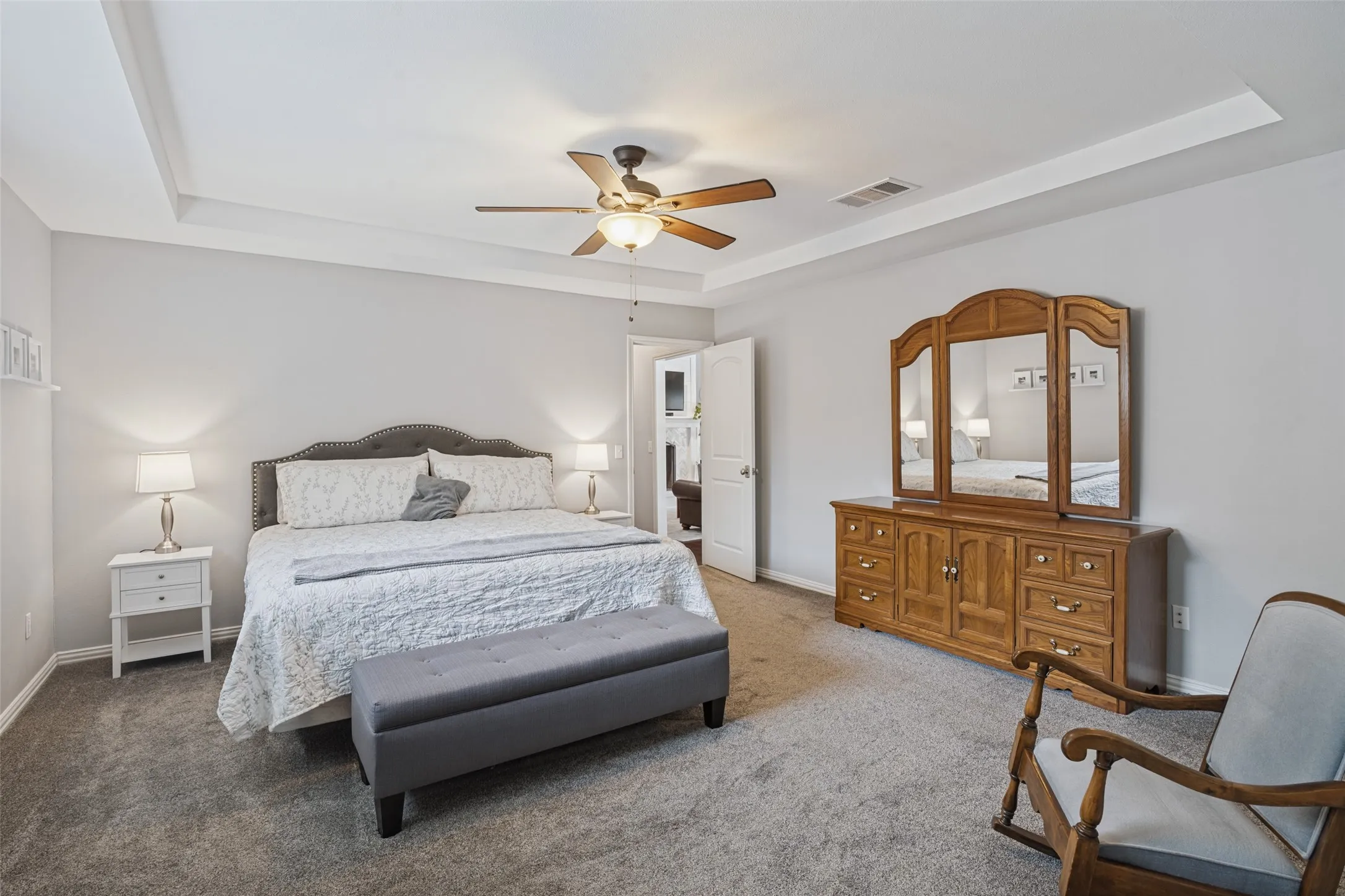 Spacious primary bedroom featuring a tray ceiling with recessed lighting and ceiling fan, carpeted flooring, and abundant natural light from multiple windows