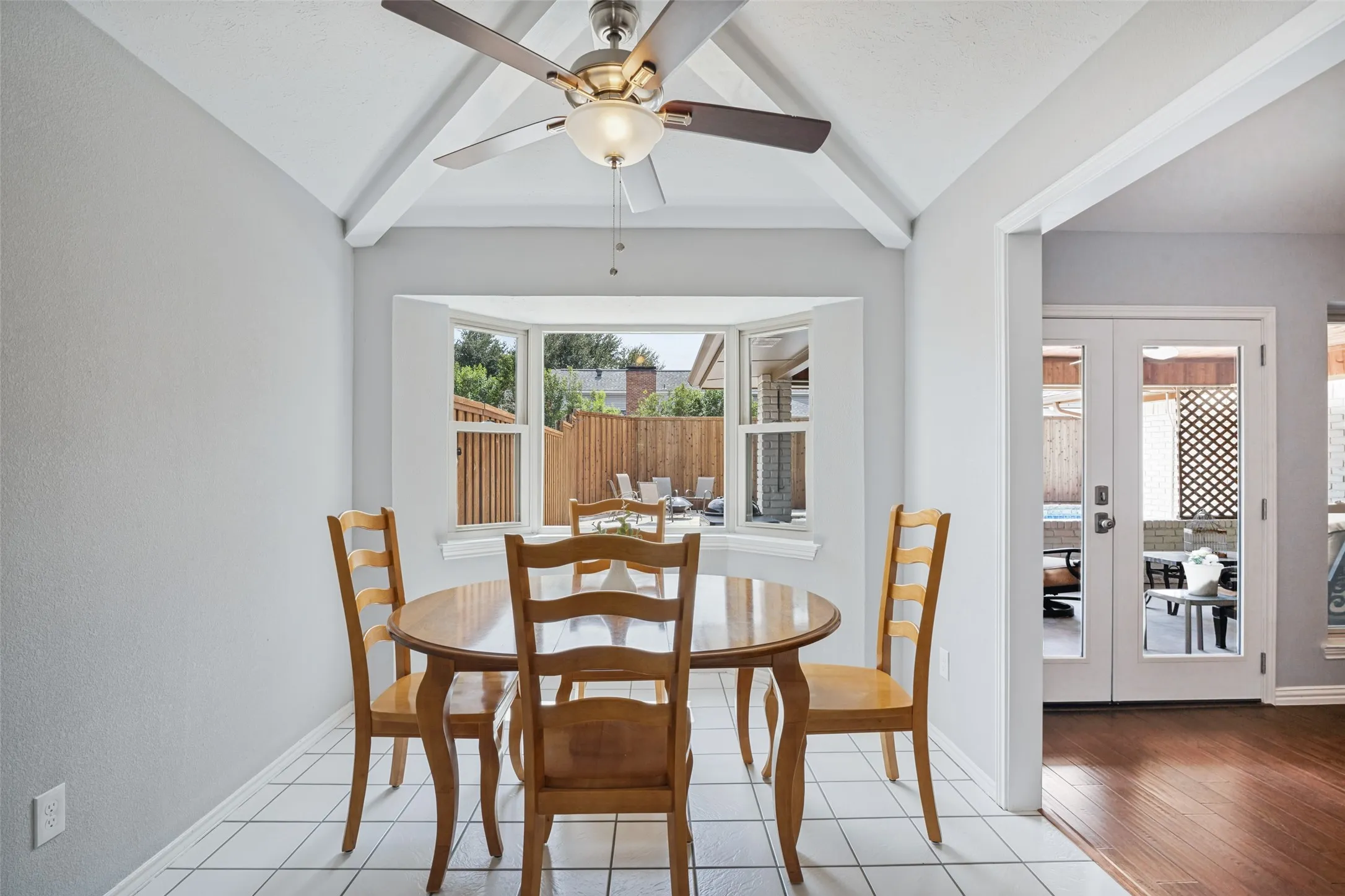 Vaulted ceiling with exposed beams, ceiling fan light fixture, bay window, white tile flooring, and double French doors with glass panels