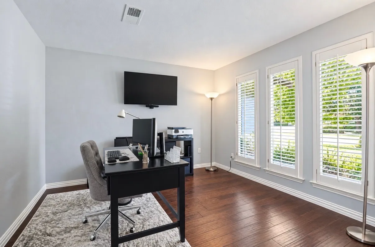 Hardwood-finish flooring, light grey wall paint, and white window shutters across multiple windows
