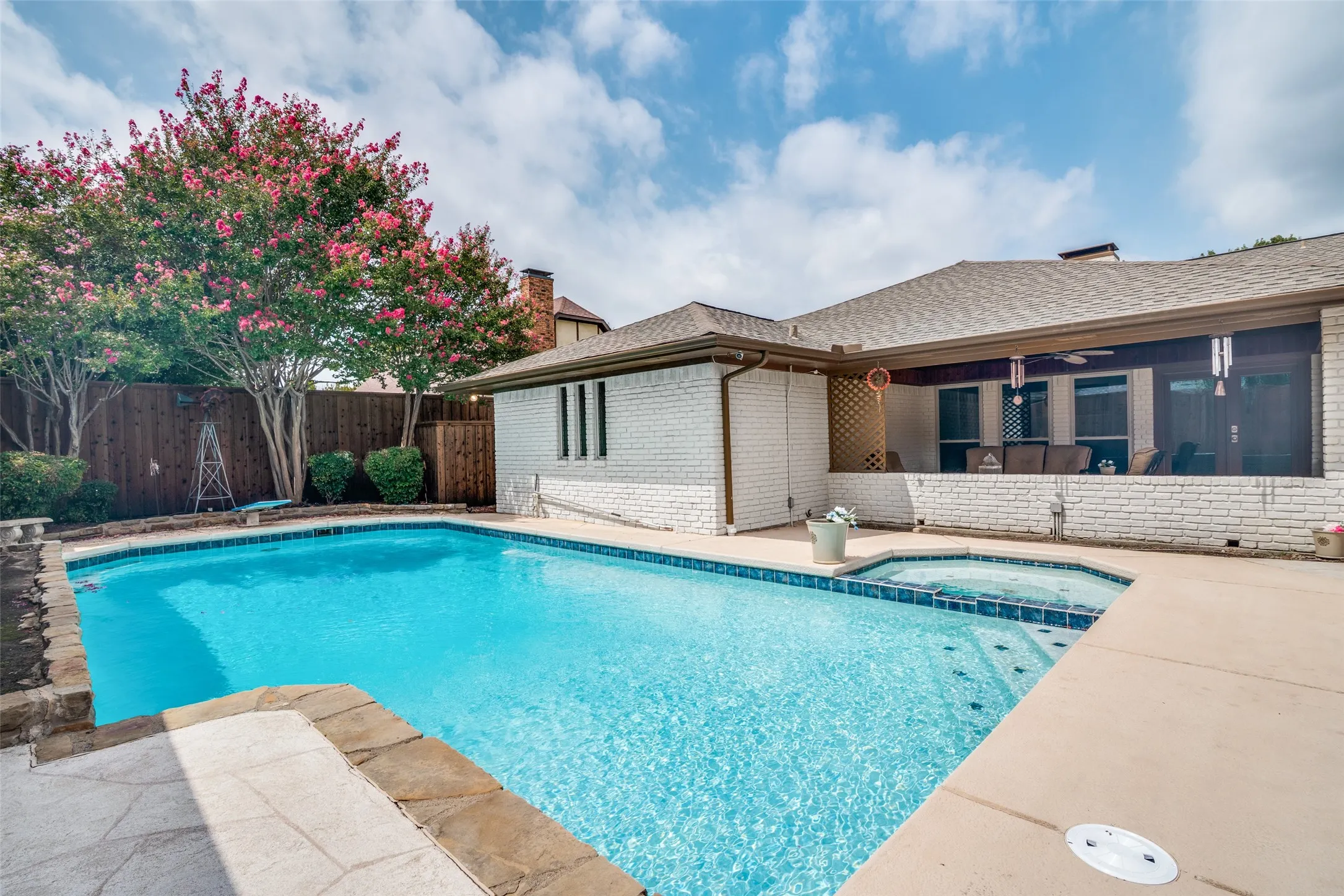 Swimming pool with integrated spa, concrete decking, wood fencing, and mature flowering trees