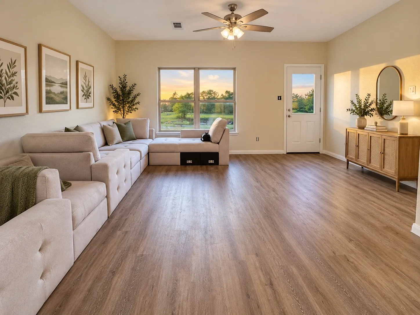 Spacious interior with wood-finish flooring, a large window, a ceiling fan with integrated lighting, and a white paneled door with a glass insert