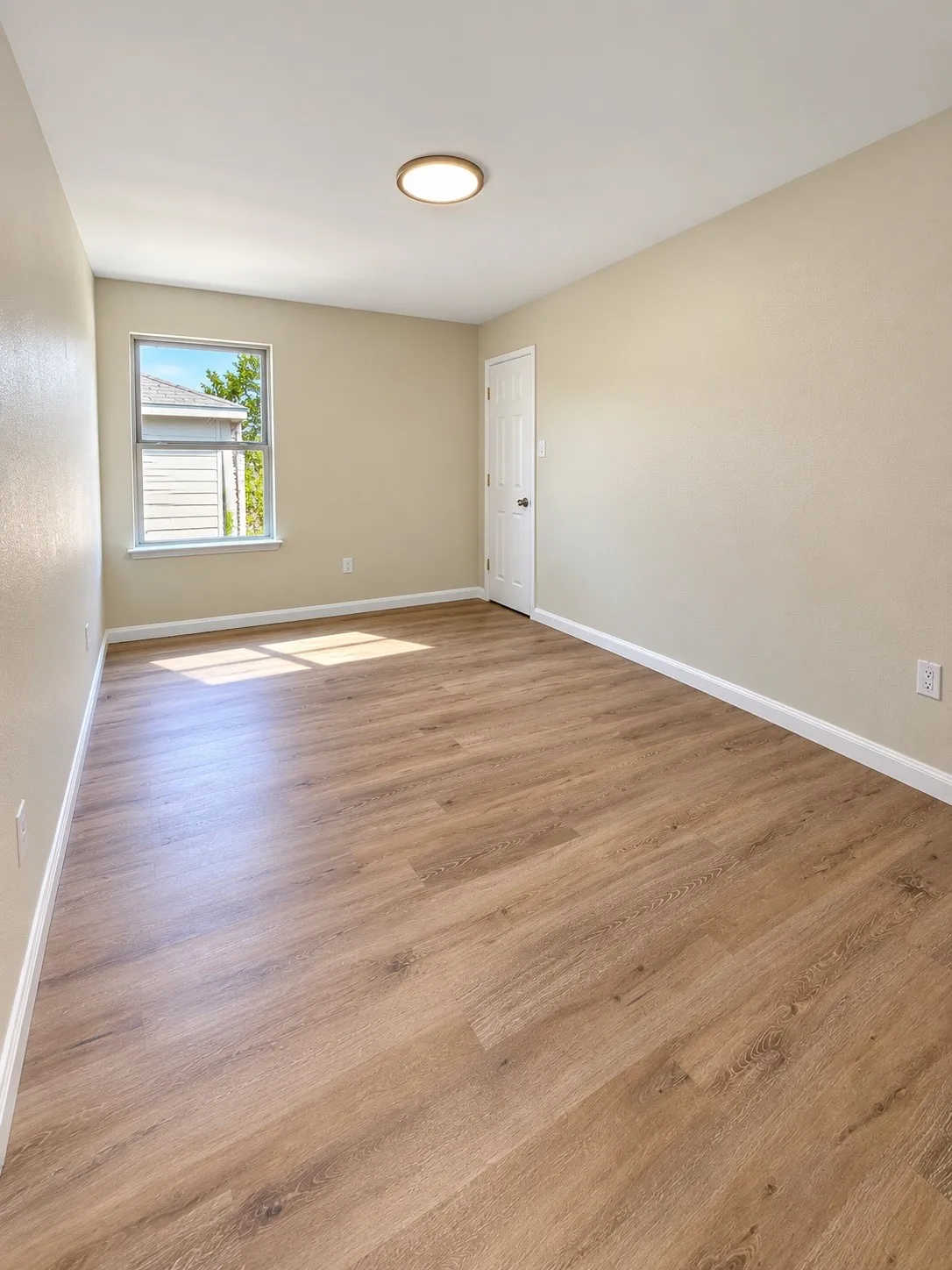 Wood-finish flooring, neutral wall paint, white trim, single window, and a flush-mount ceiling light