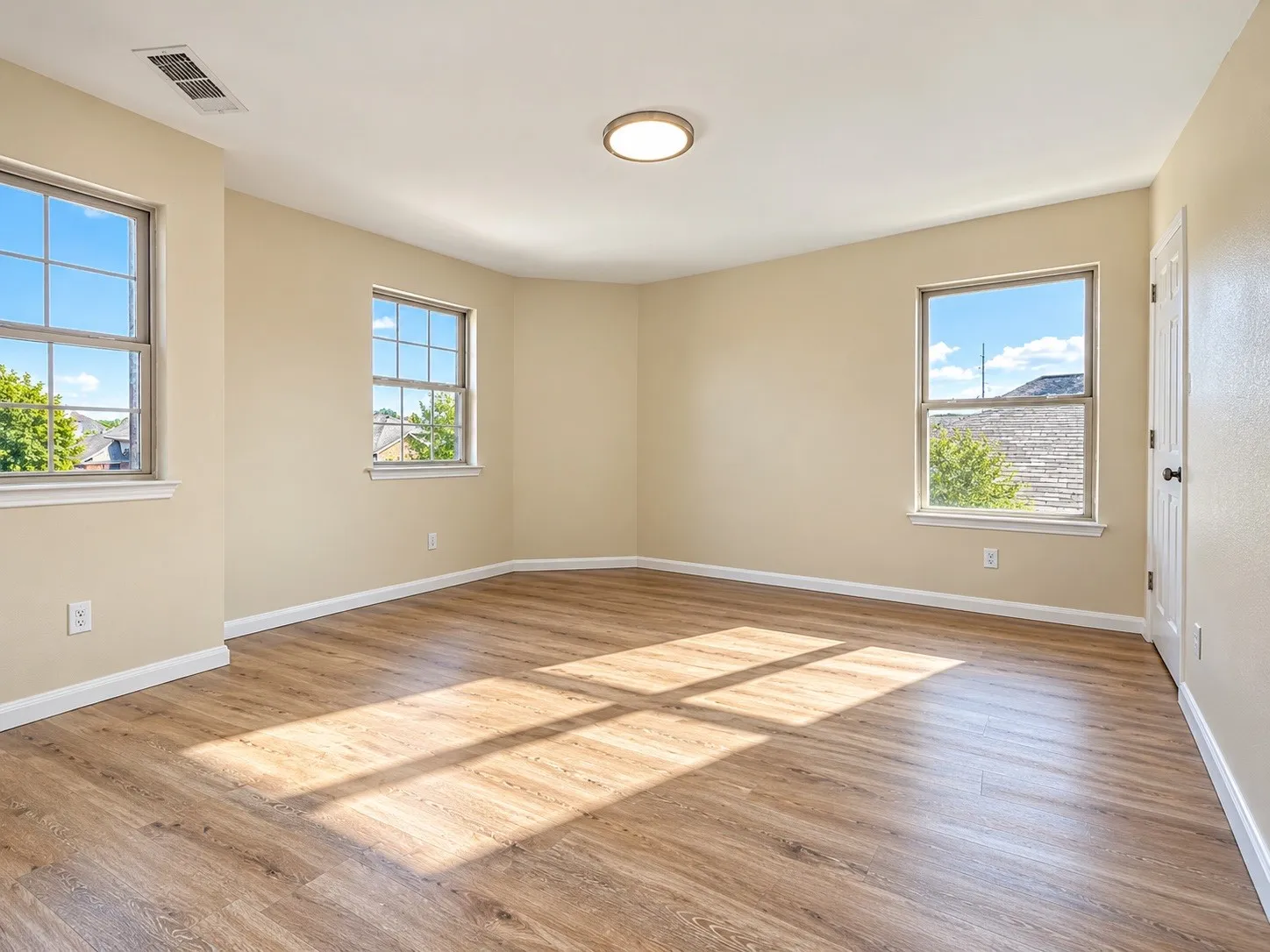 Spacious room featuring wood-finish flooring, three double-hung windows, a flush-mount ceiling light, and neutral wall tones