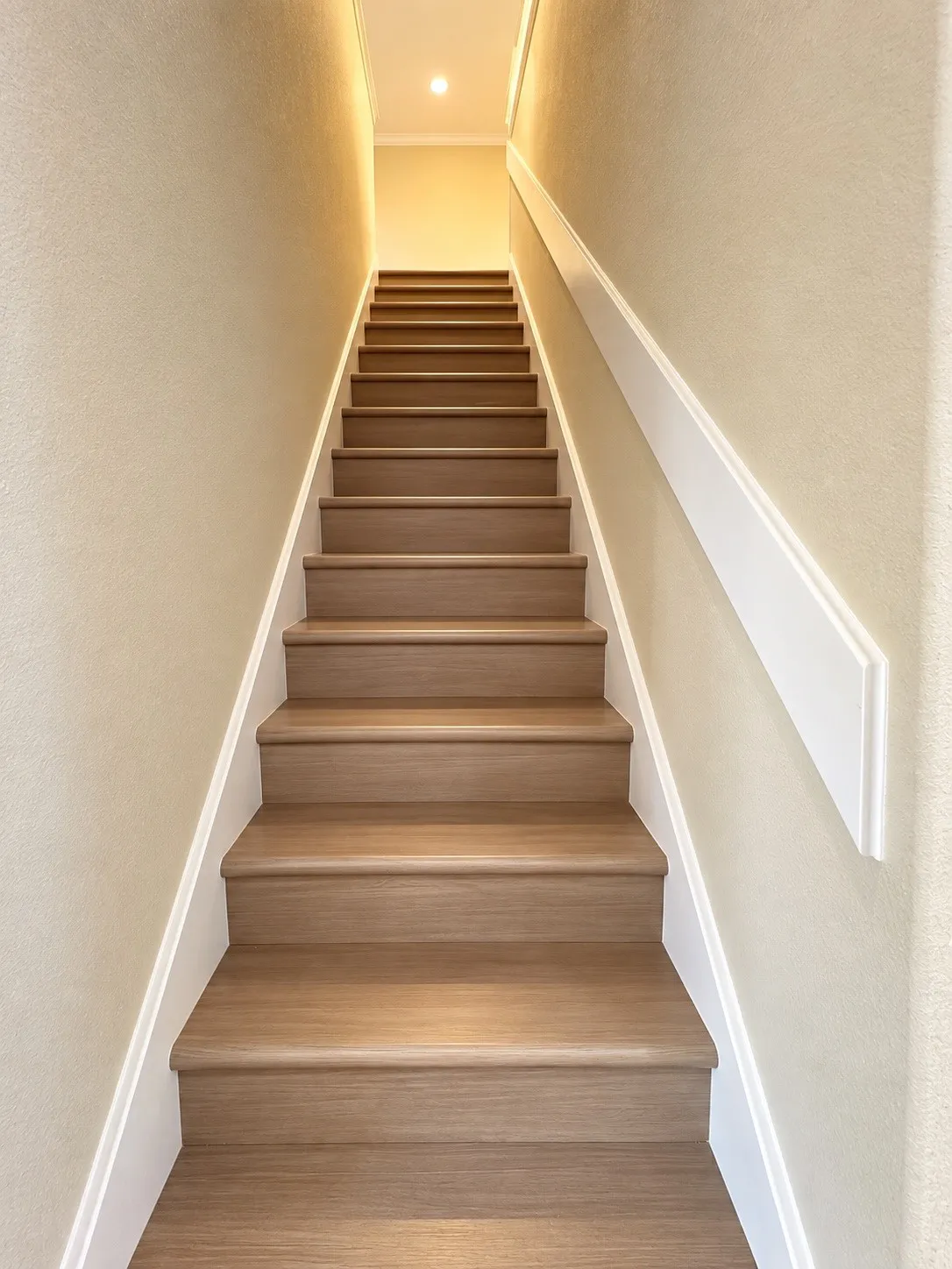 Staircase with wood-finish treads, white risers, and a wall-mounted handrail