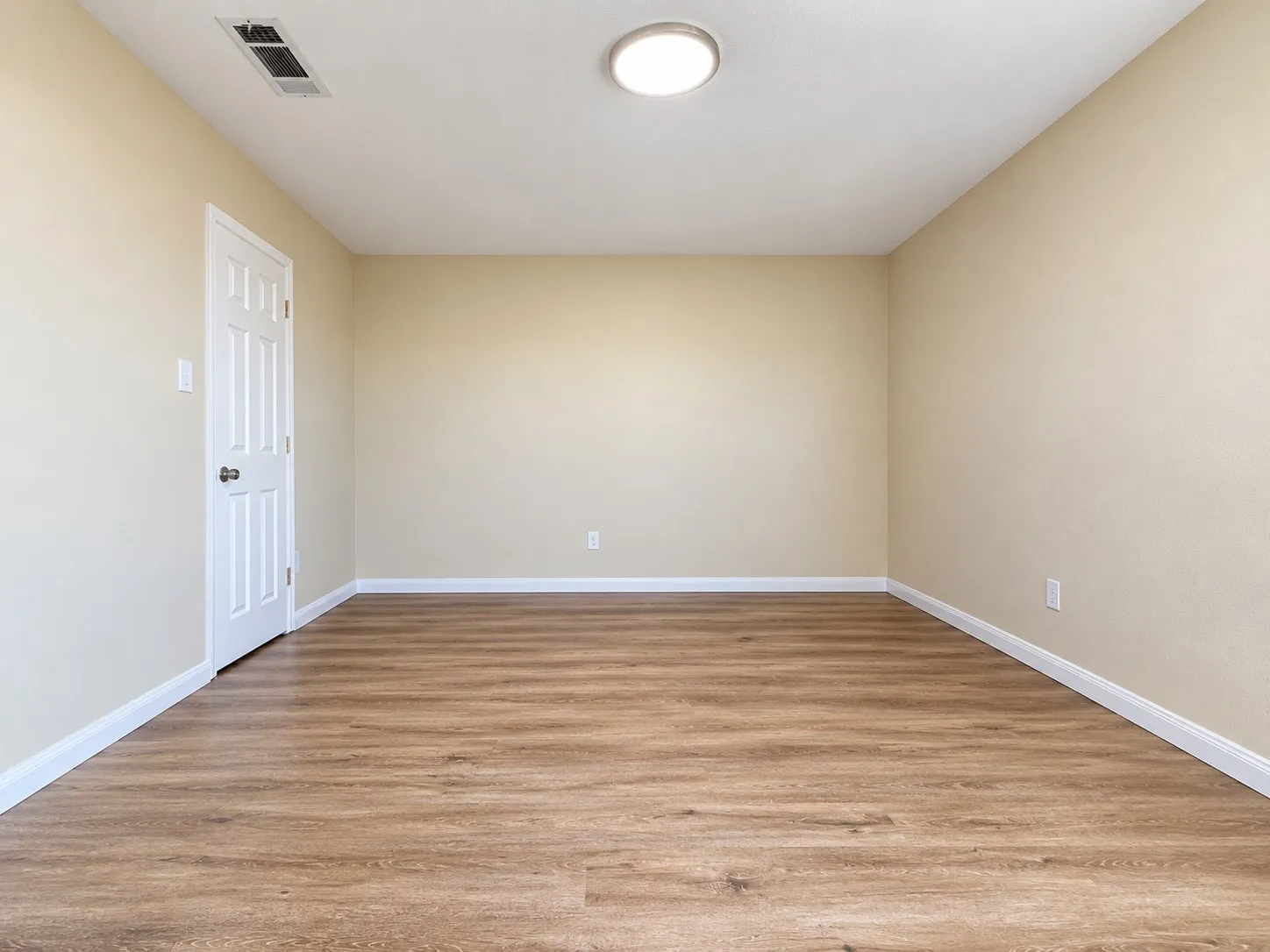 Wood-finish flooring, neutral wall tones, white trim, and a flush-mount ceiling light