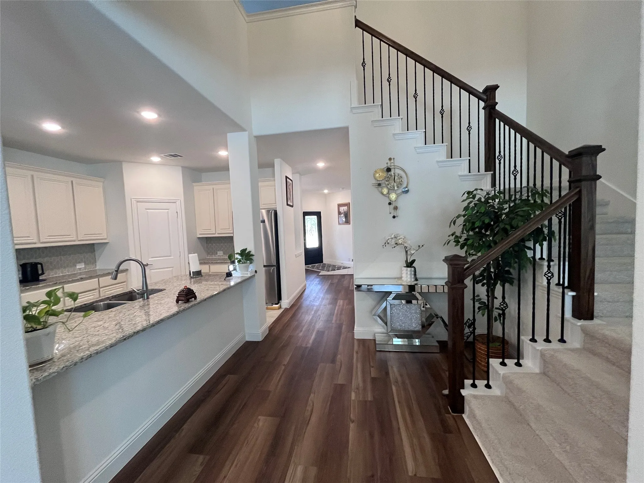 Hardwood-style flooring throughout, kitchen with granite countertops, white cabinetry, stainless steel sink, recessed lighting, and a staircase with wrought iron balusters