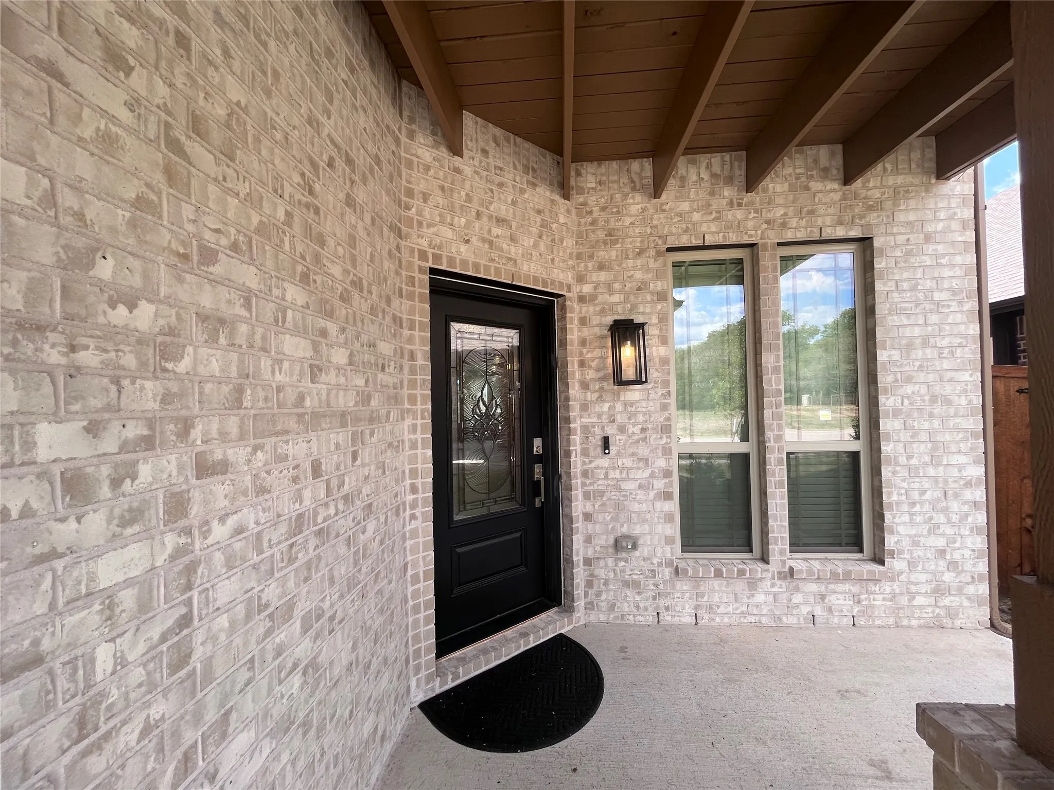 Brick exterior with a covered entry, decorative glass front door, exterior wall lantern, and concrete patio
