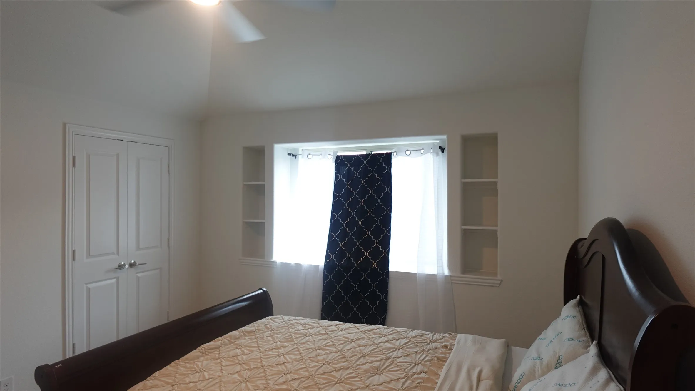 Bedroom 4 with built-in shelving flanking a window recess, white paneled bifold closet doors, and a ceiling fan