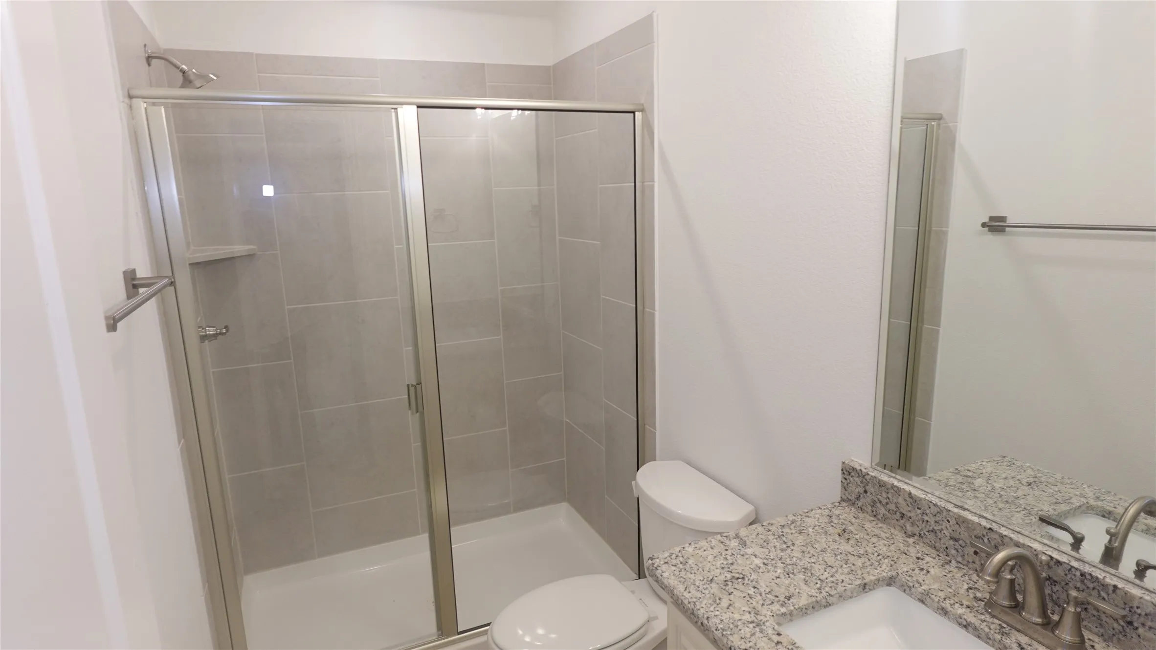 Shower with sliding glass enclosure, light gray tile surround, and built-in shelving