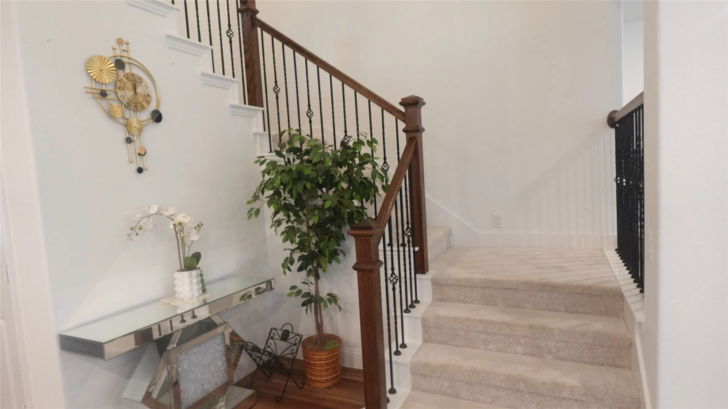 Staircase with carpeted treads, wood handrail, and wrought iron balusters