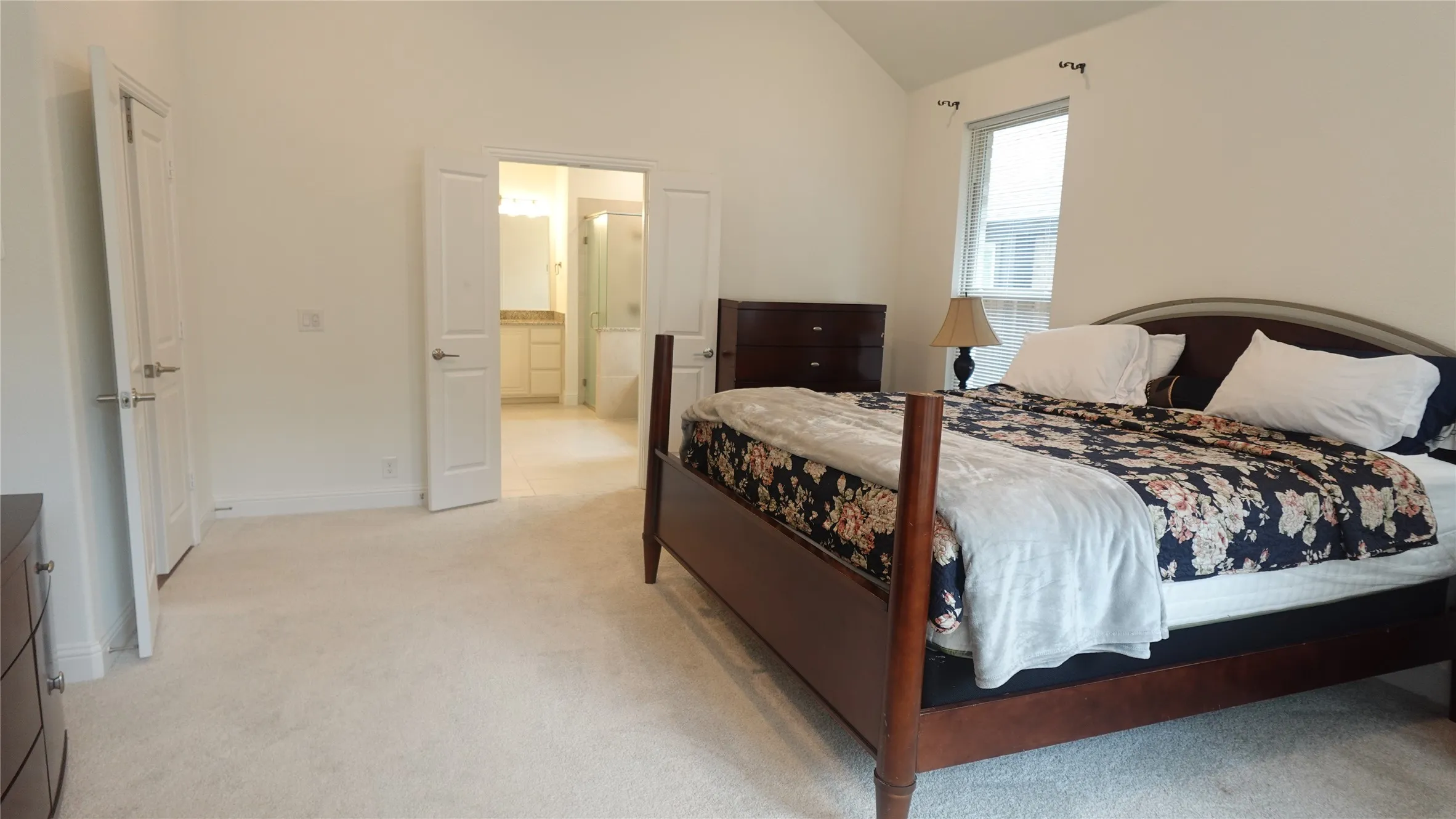 Vaulted ceiling bedroom with carpet flooring, double-door entry to a bathroom, a window, and a built-in closet with double doors