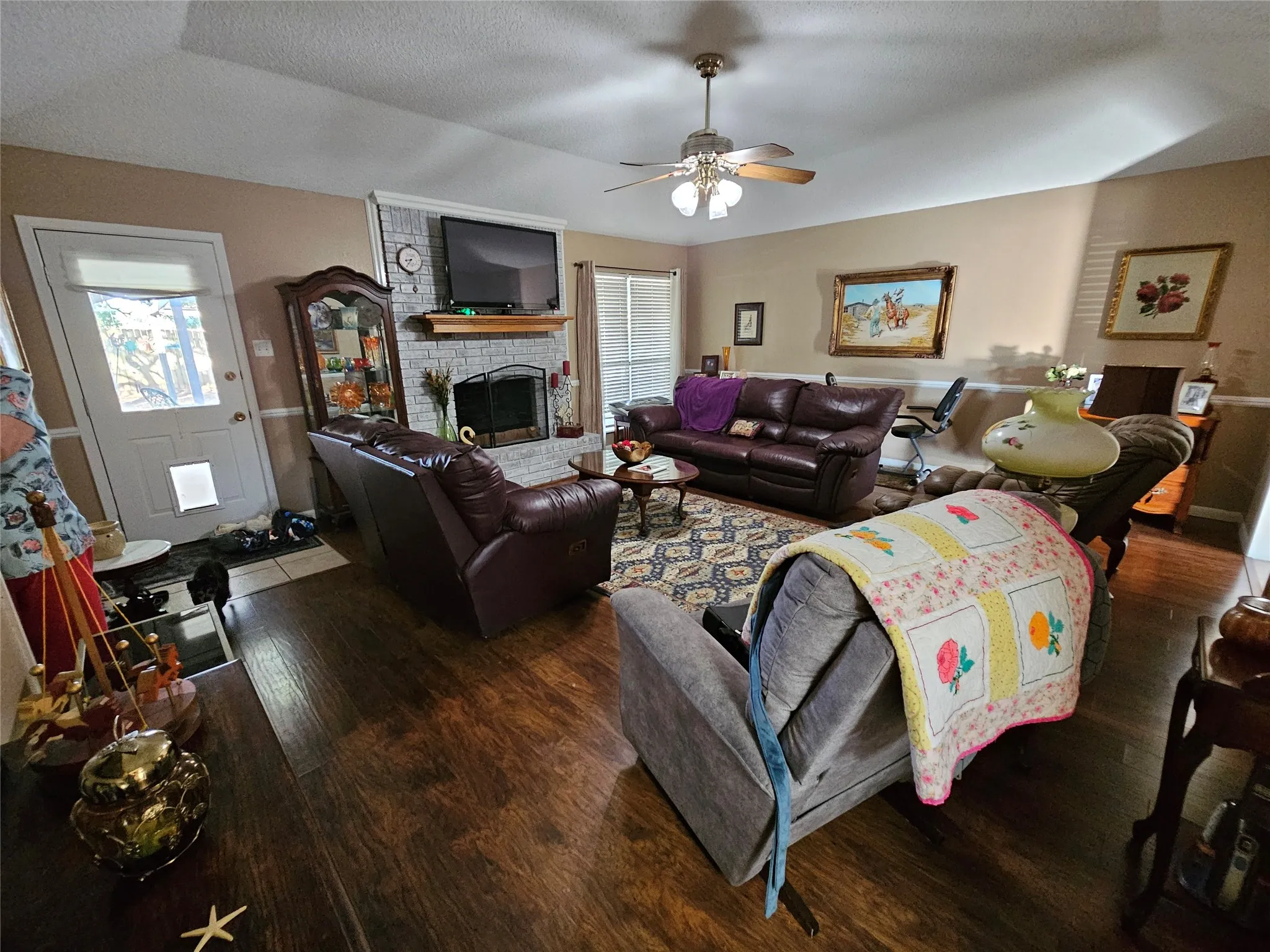 Living Room with hardwood-finish flooring, a ceiling fan with integrated lighting, and a fireplace with a stone surround and wood mantel