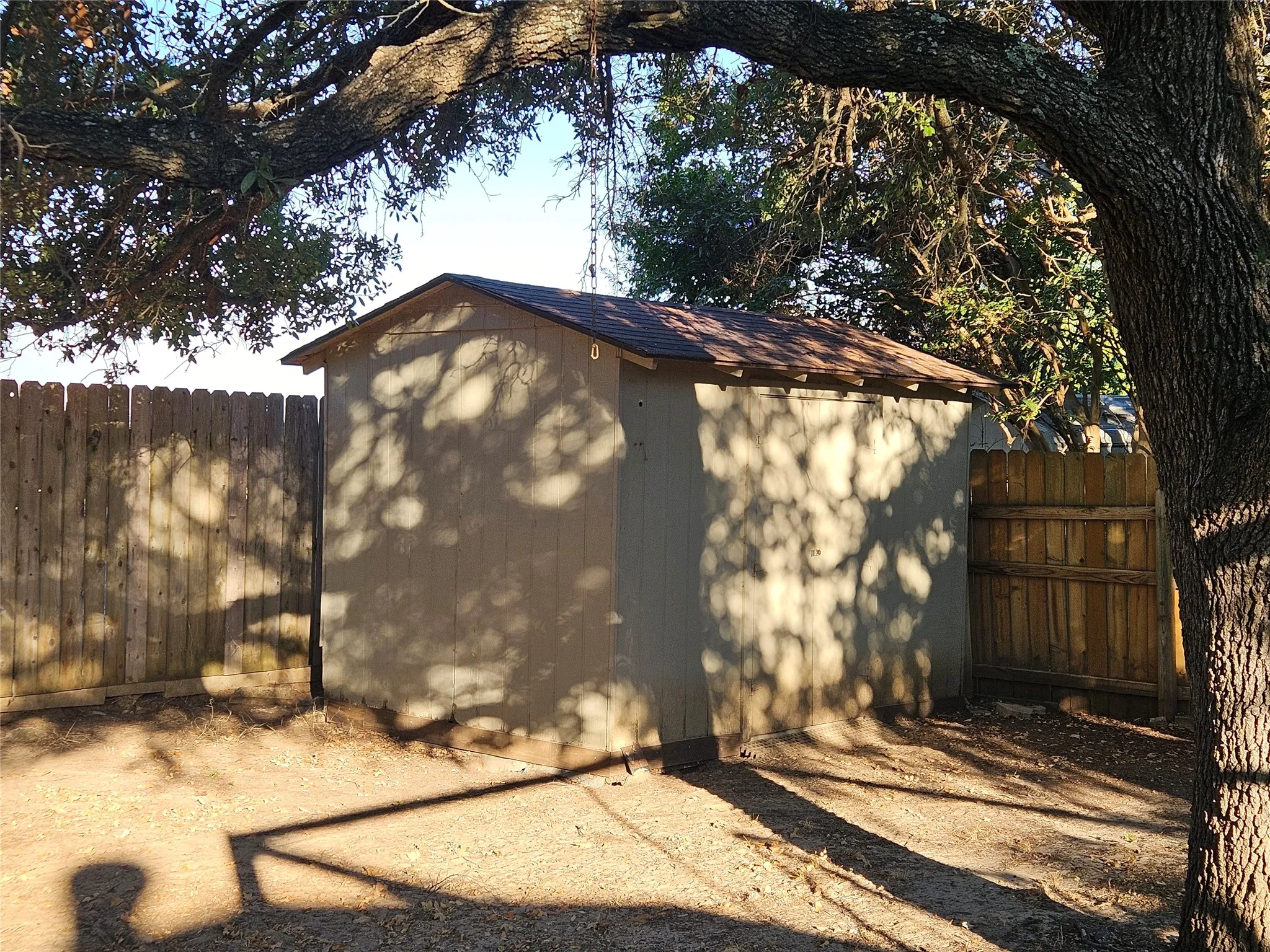 Wood-sided 8x12 storage shed with a shingled roof, surrounded by wood fencing and mature trees