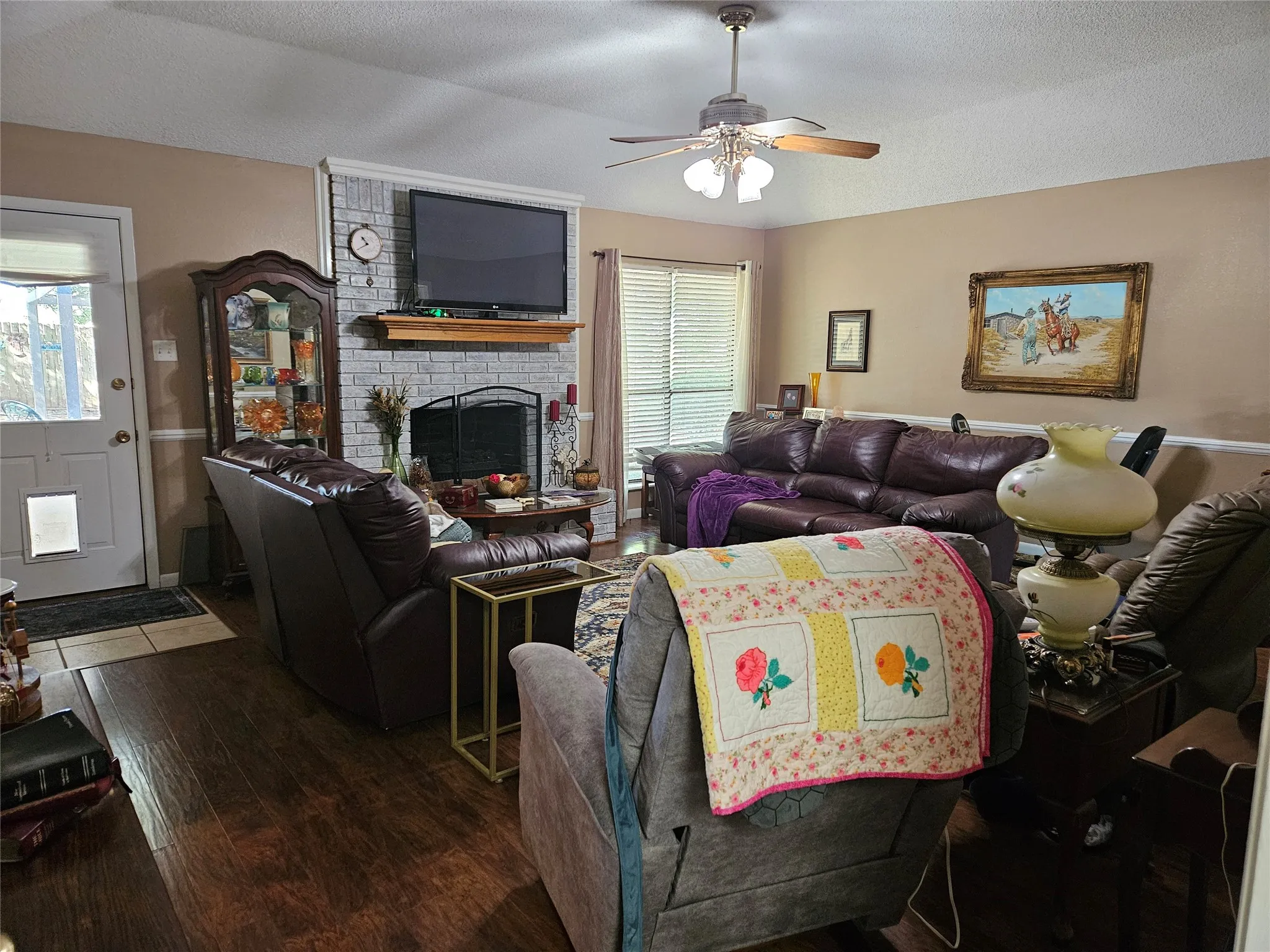 Wood-finish flooring, white trim details, ceiling fan with integrated lighting, fireplace with a stone surround, and a wooden mantel