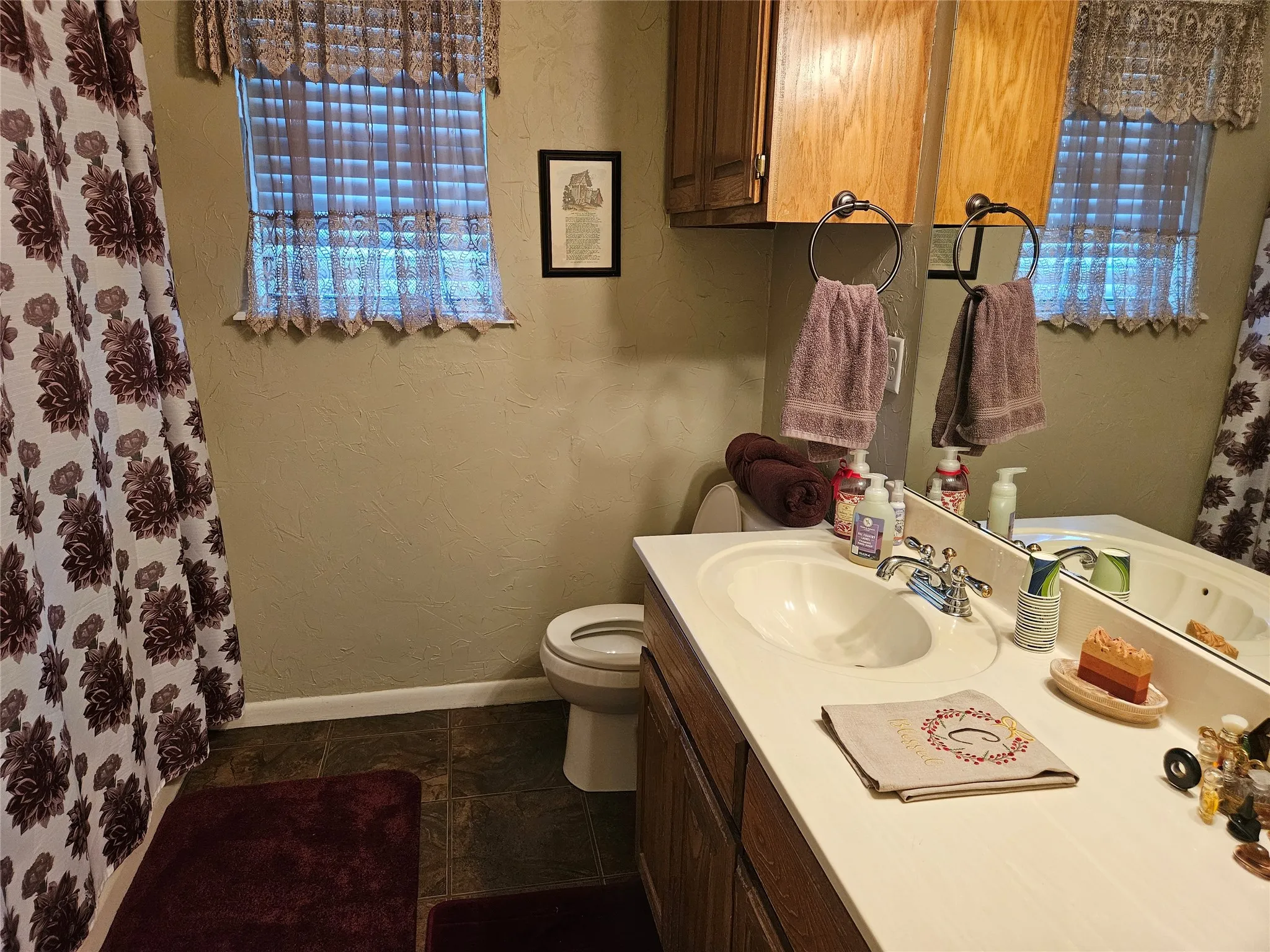 Vanity with integrated sink, wood-finish cabinetry, and overhead wood-finish storage